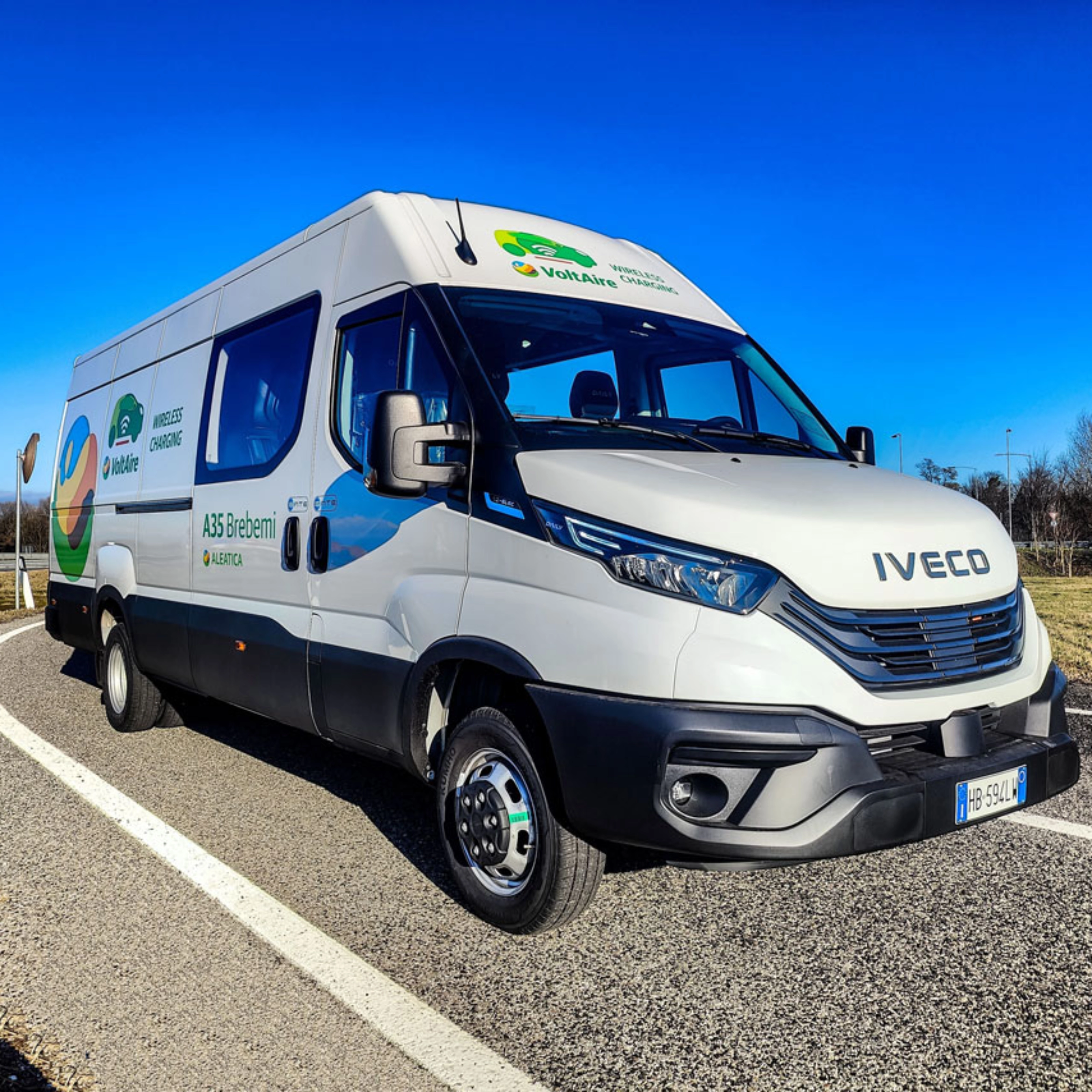 Ein weißer Iveco-Transporter fährt auf einer kurvigen Straße bei blauem Himmel.