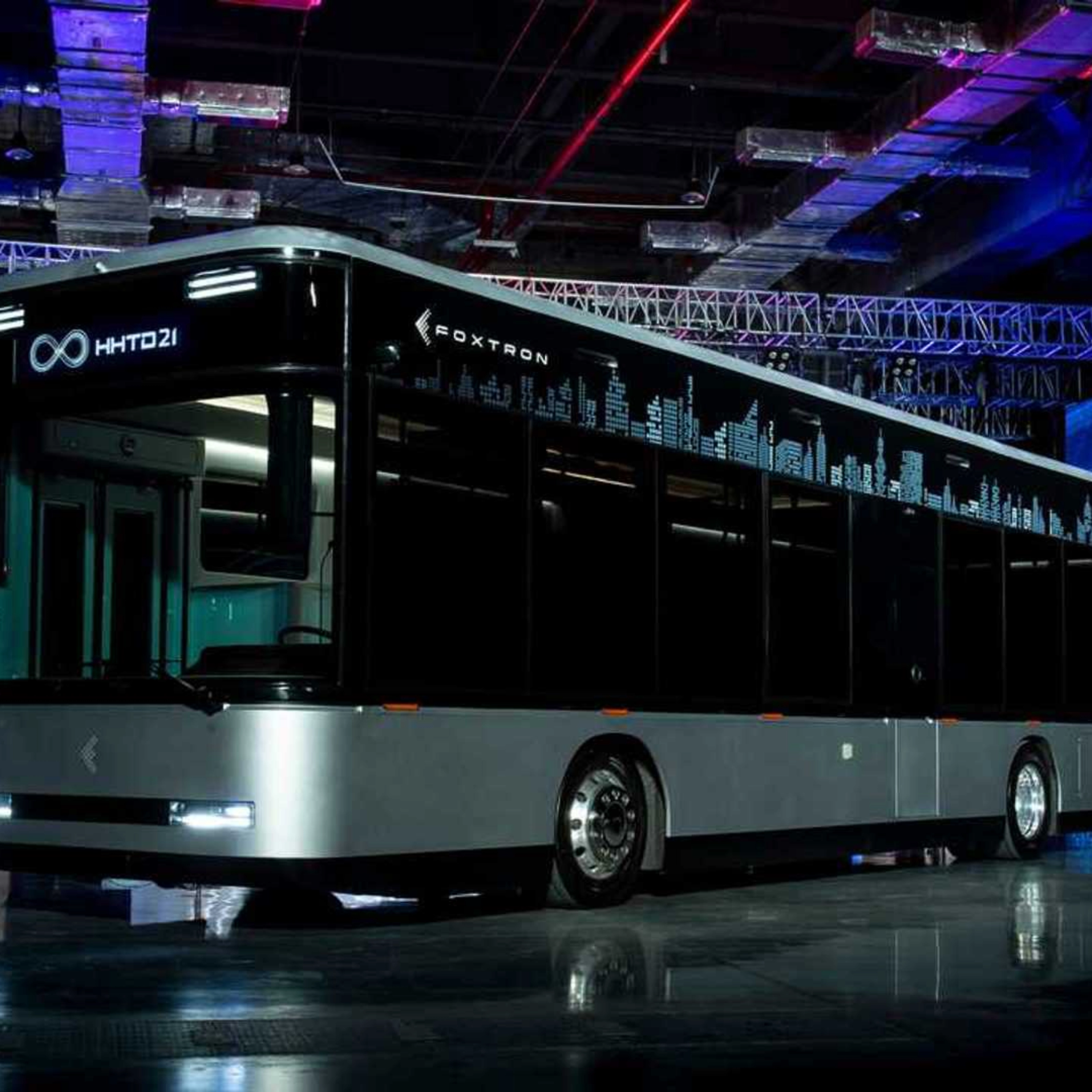 A modern electric city bus is showcased indoors with the logo "Foxtron" and digital skyline.