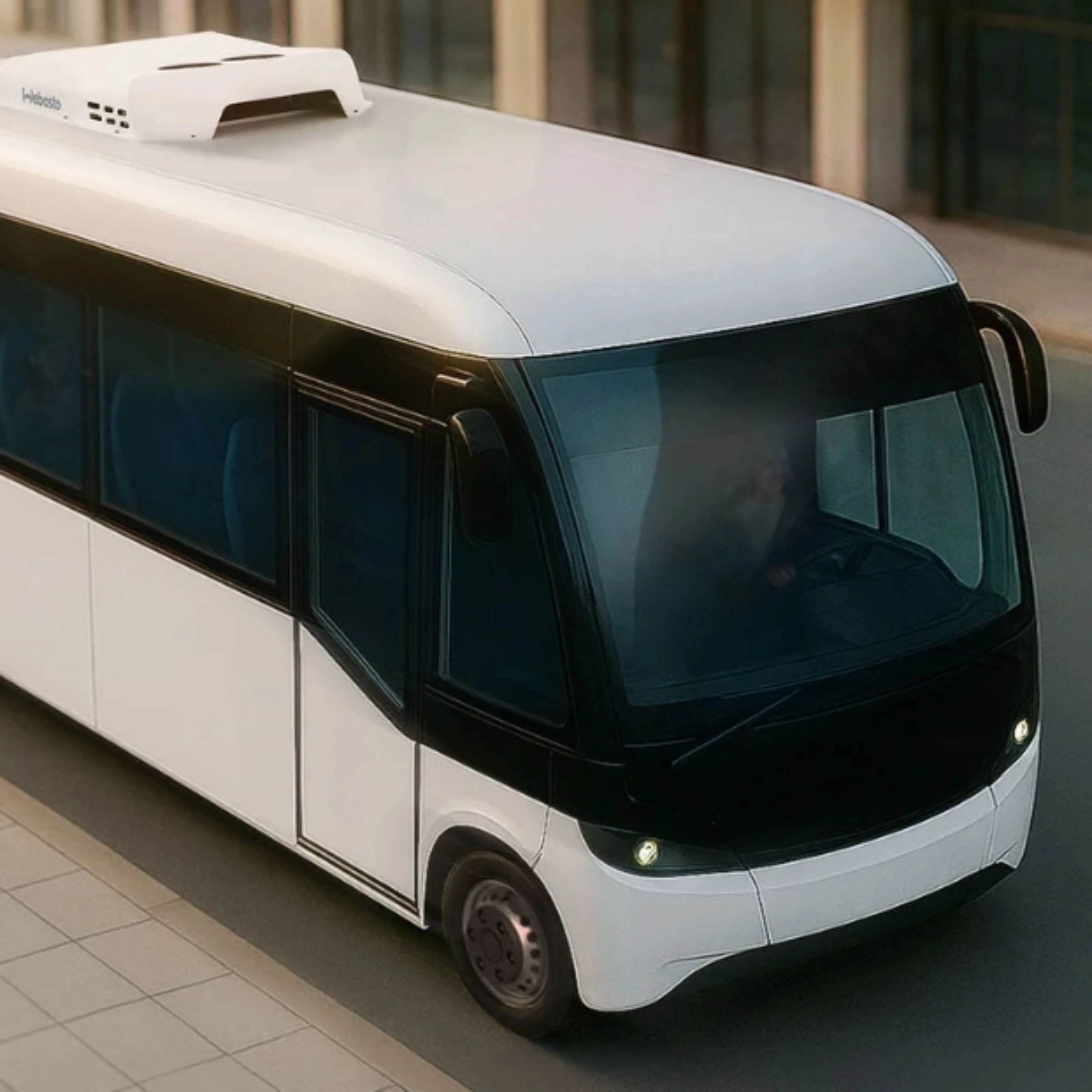 Small white autonomous shuttle bus driving on a city street, viewed from above.