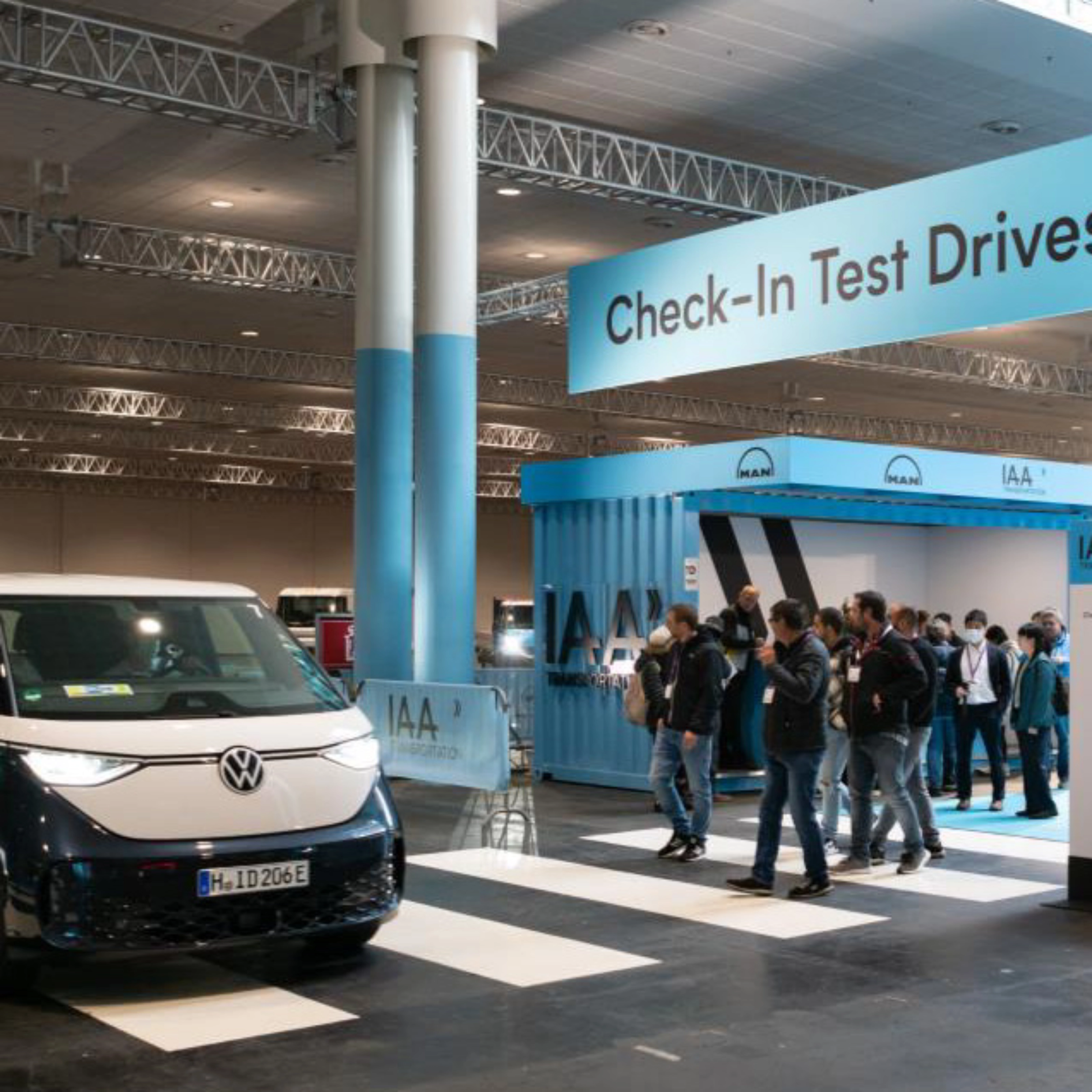 Exhibition hall scene with a Volkswagen van driving past the IAA Transportation check-in for test drives.