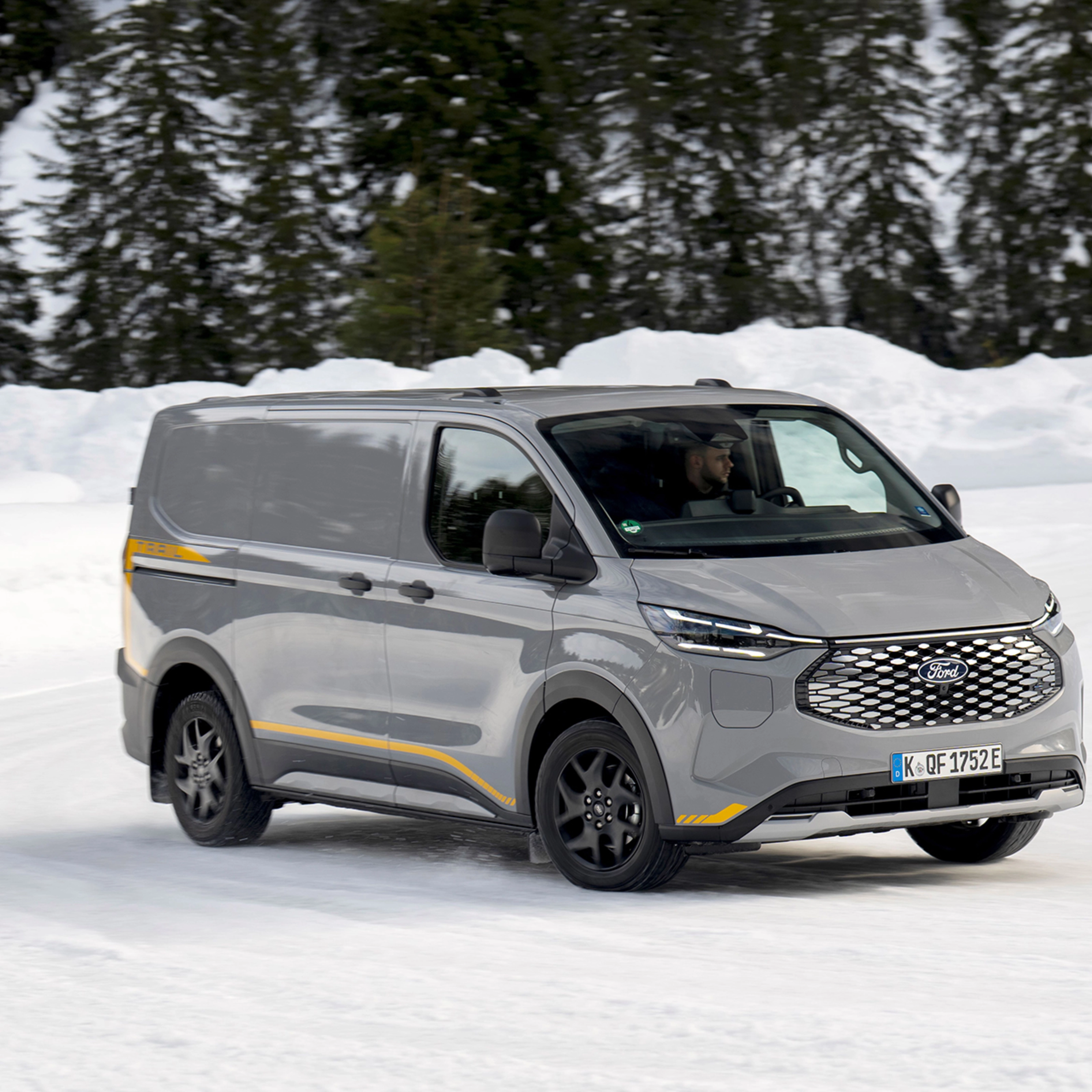 Grey Ford electric van driving on a snowy road with forest in the background.