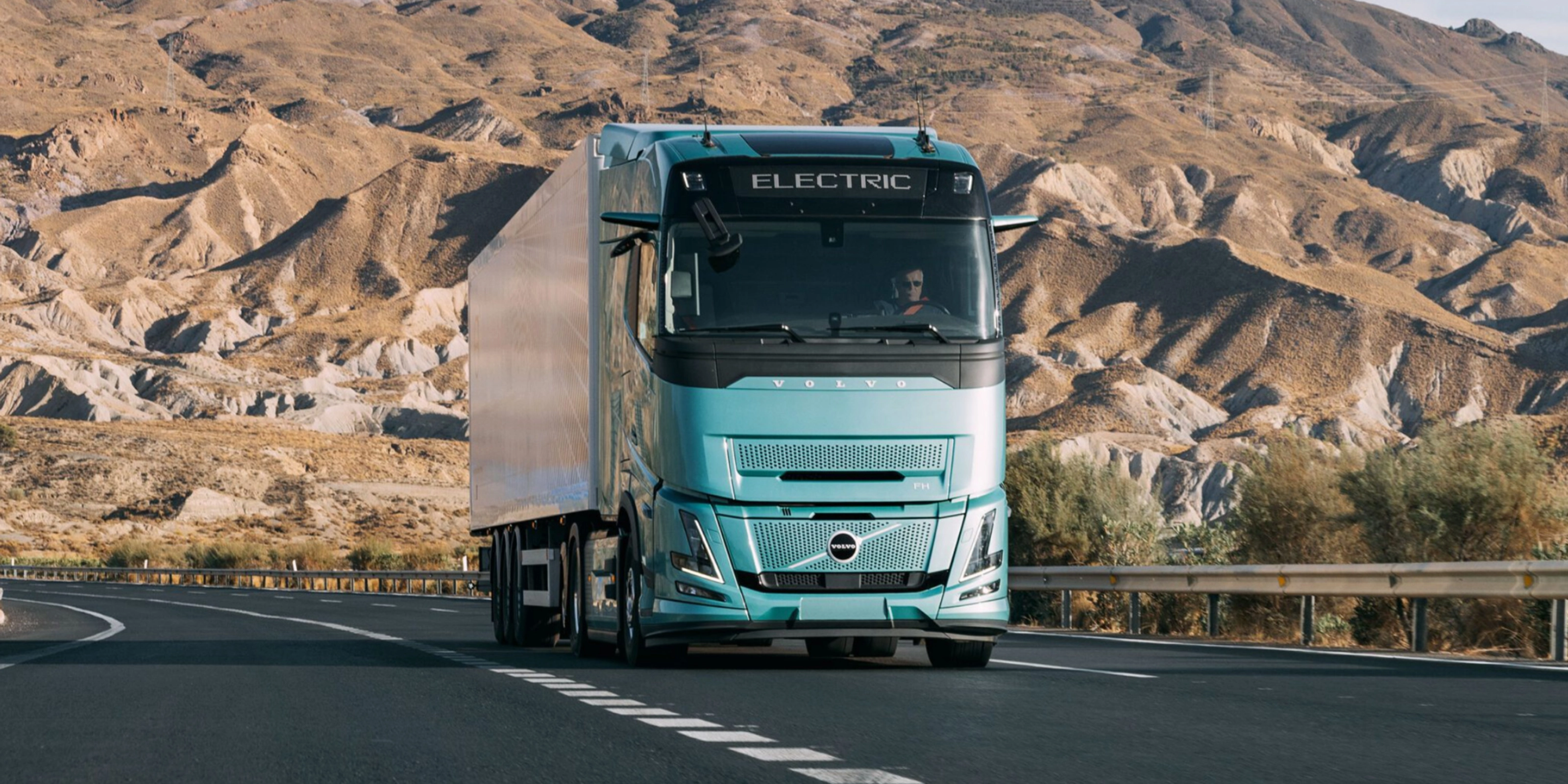 Volvo truck driving on a highway through a rocky desert landscape.
