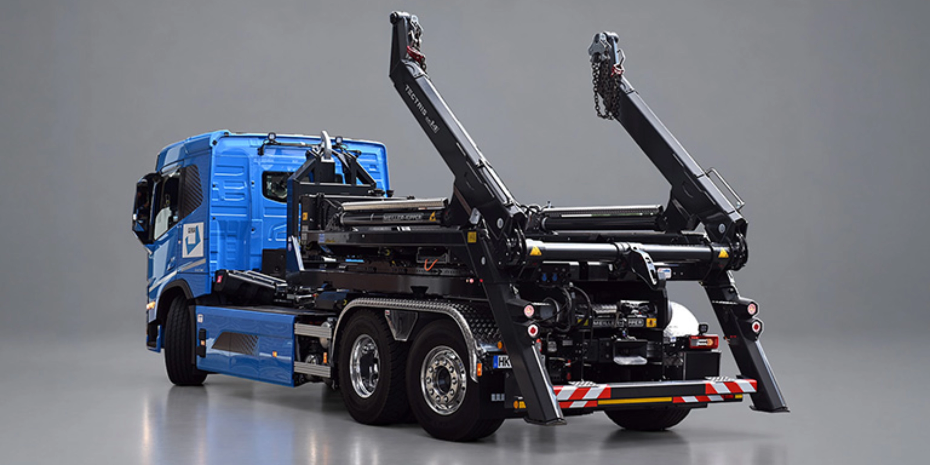 Blauer Lkw mit schwarzem Meiller-Hakenliftsystem und angehobenen Hubarmen in schräger Rückansicht.