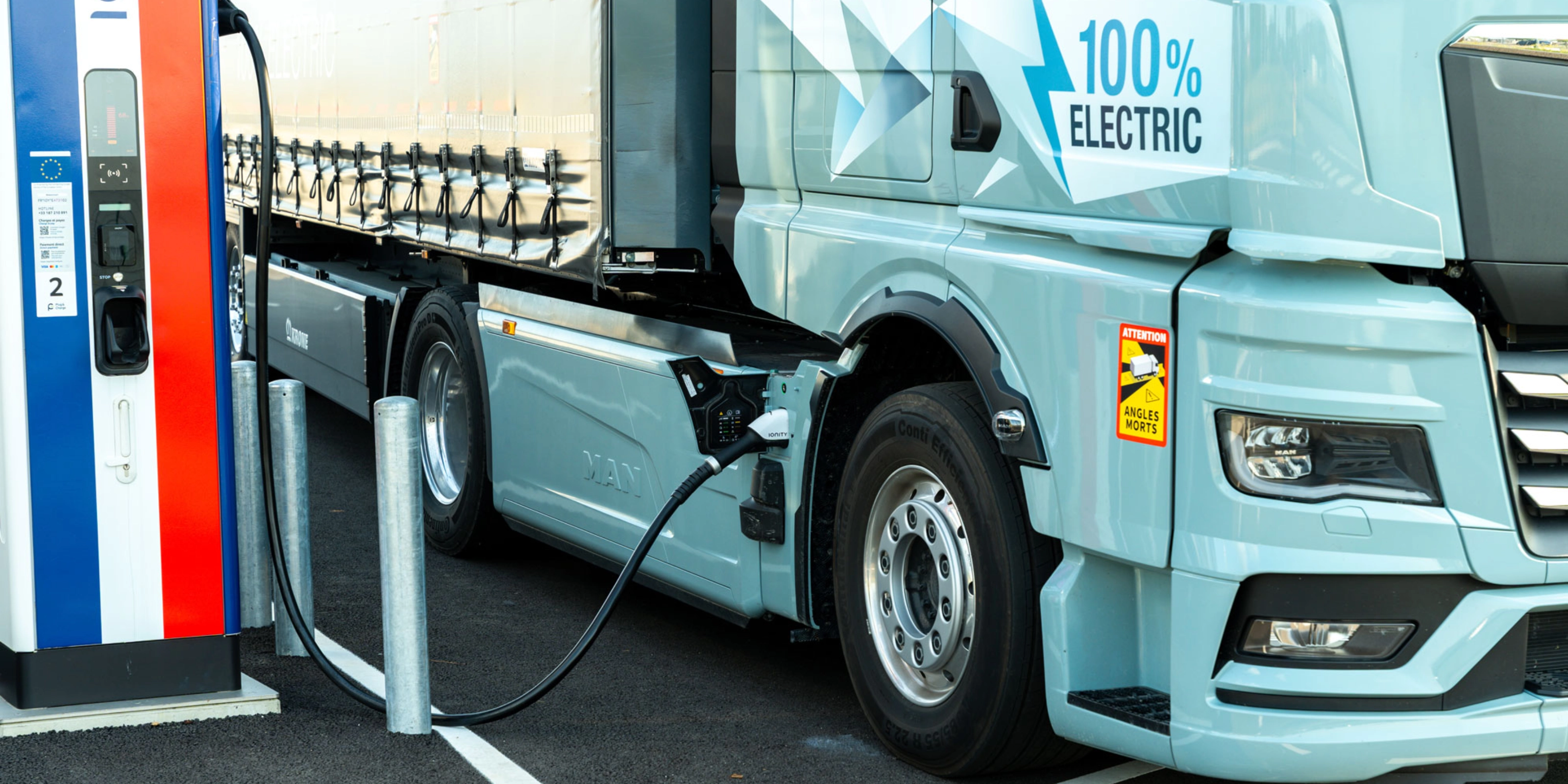 Electric truck charging at a public station, labeled 100% electric.