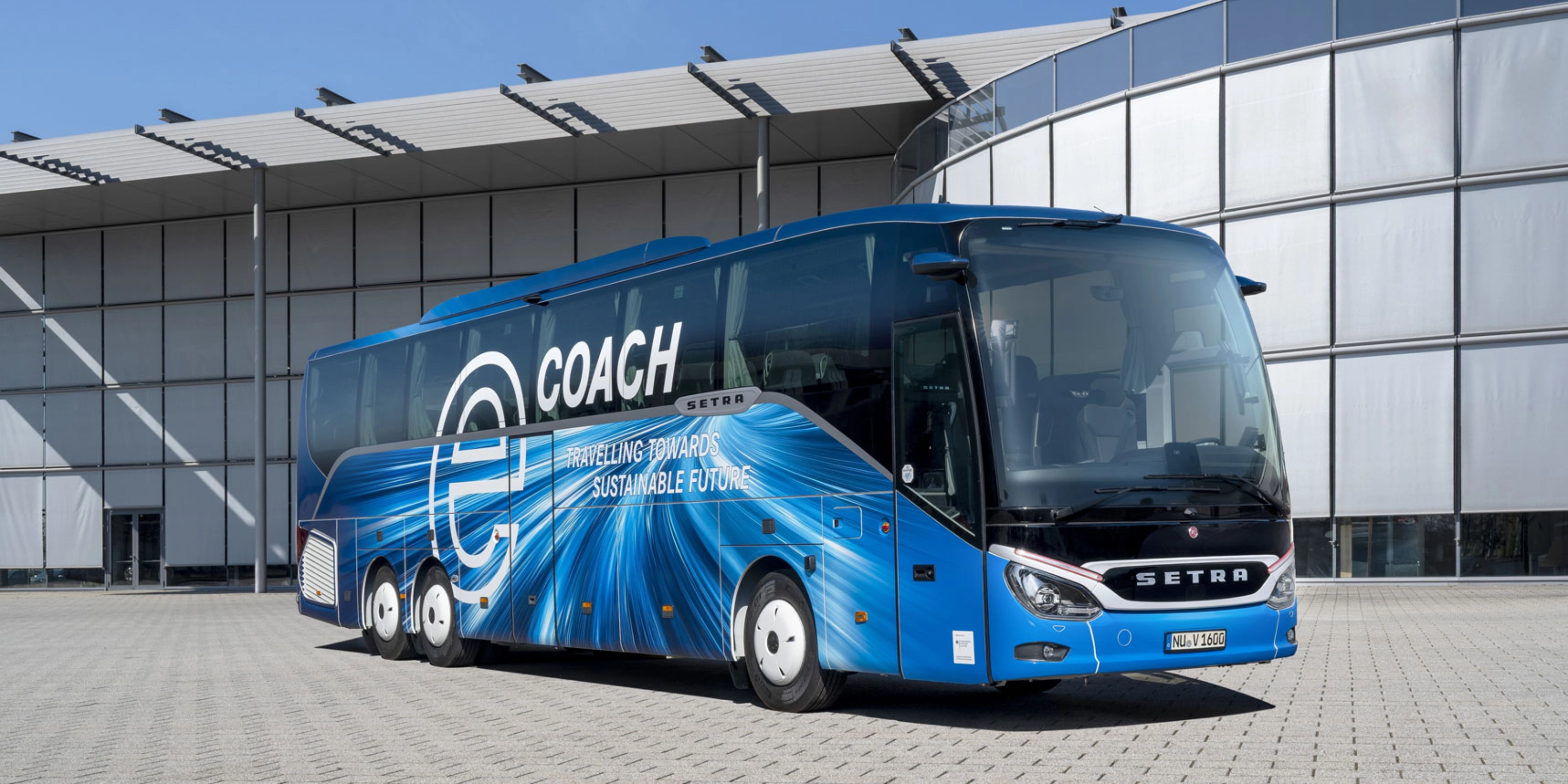 Blauer Setra-Reisebus mit Nachhaltigkeits-Slogan vor modernem Gebäude.
