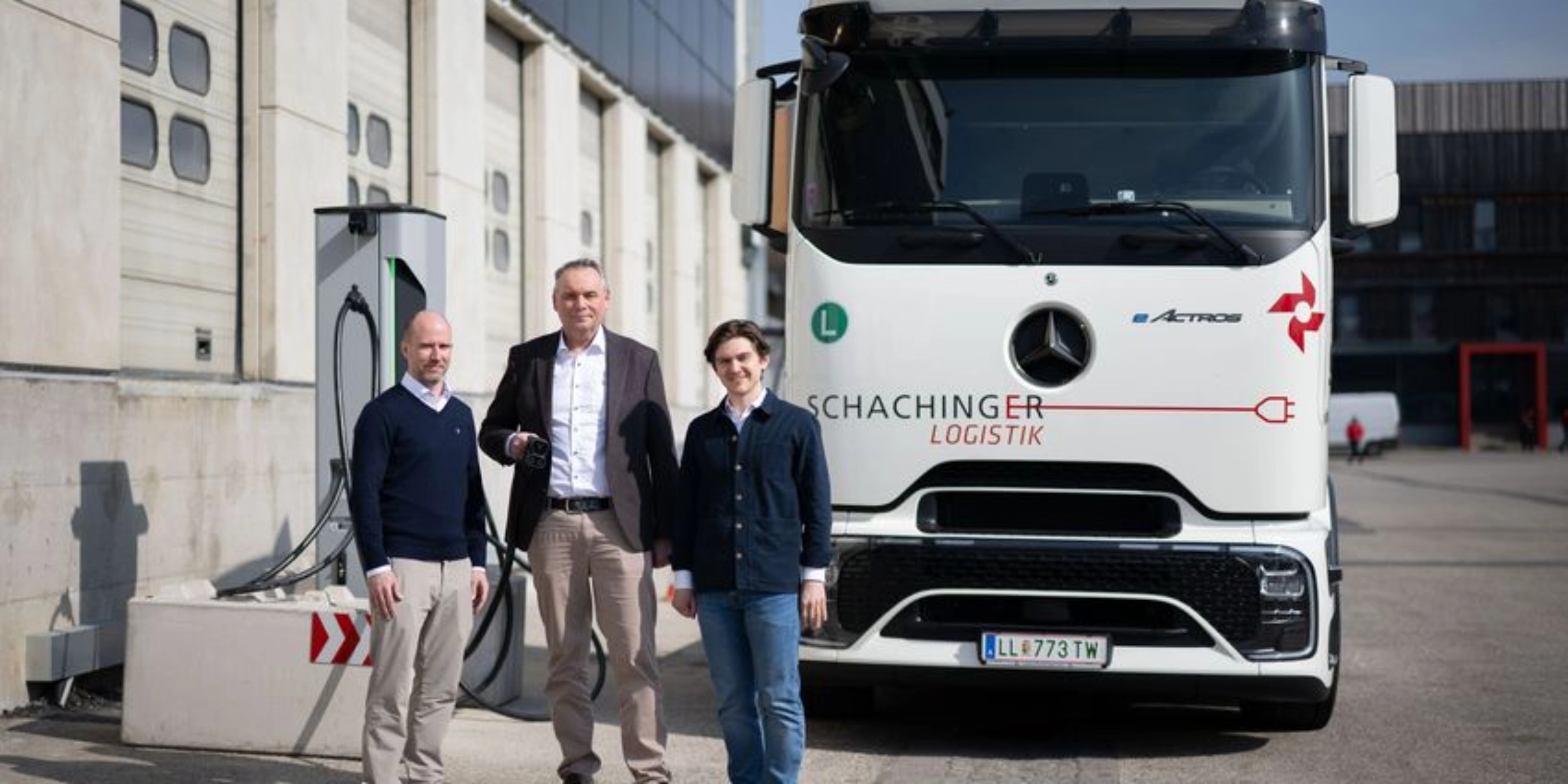 Three men standing in front of a white truck outside an industrial building.