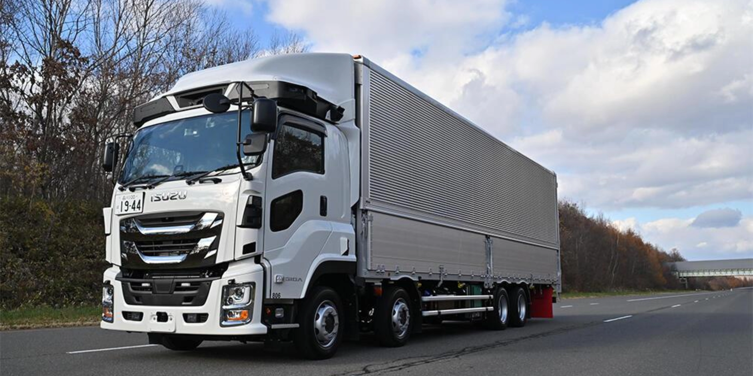 White semi-truck with trailer driving on a highway under a cloudy sky.