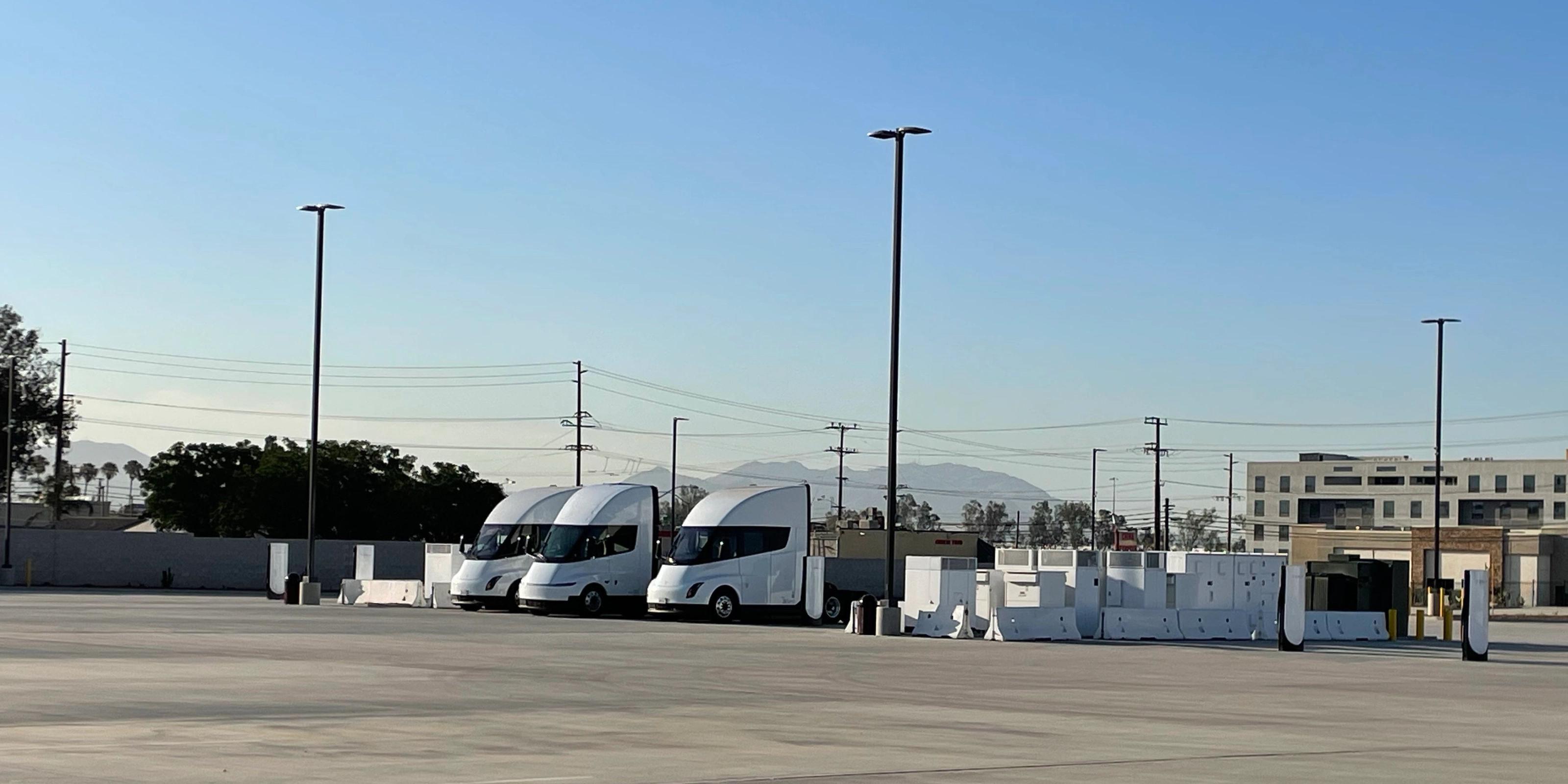 Three white electric trucks are parked at a charging station.
