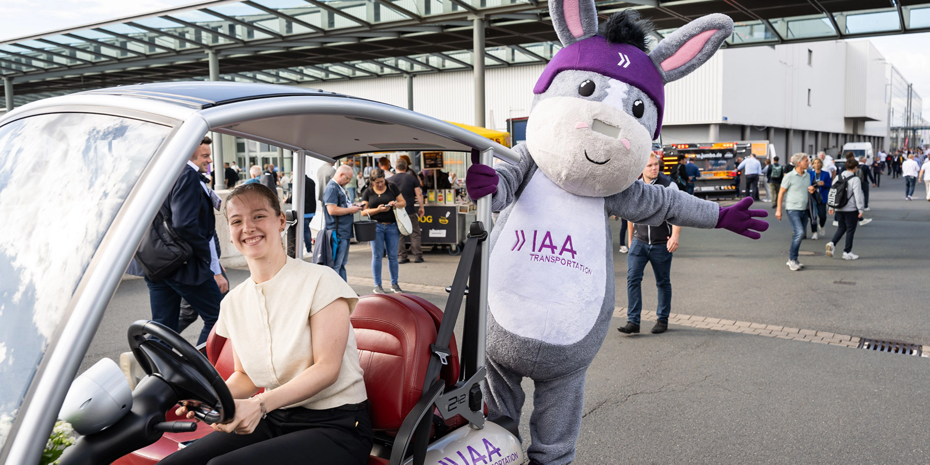 Frau in einem IAA-Fahrzeug neben dem IAA Transportation Maskottchen auf der Messe.