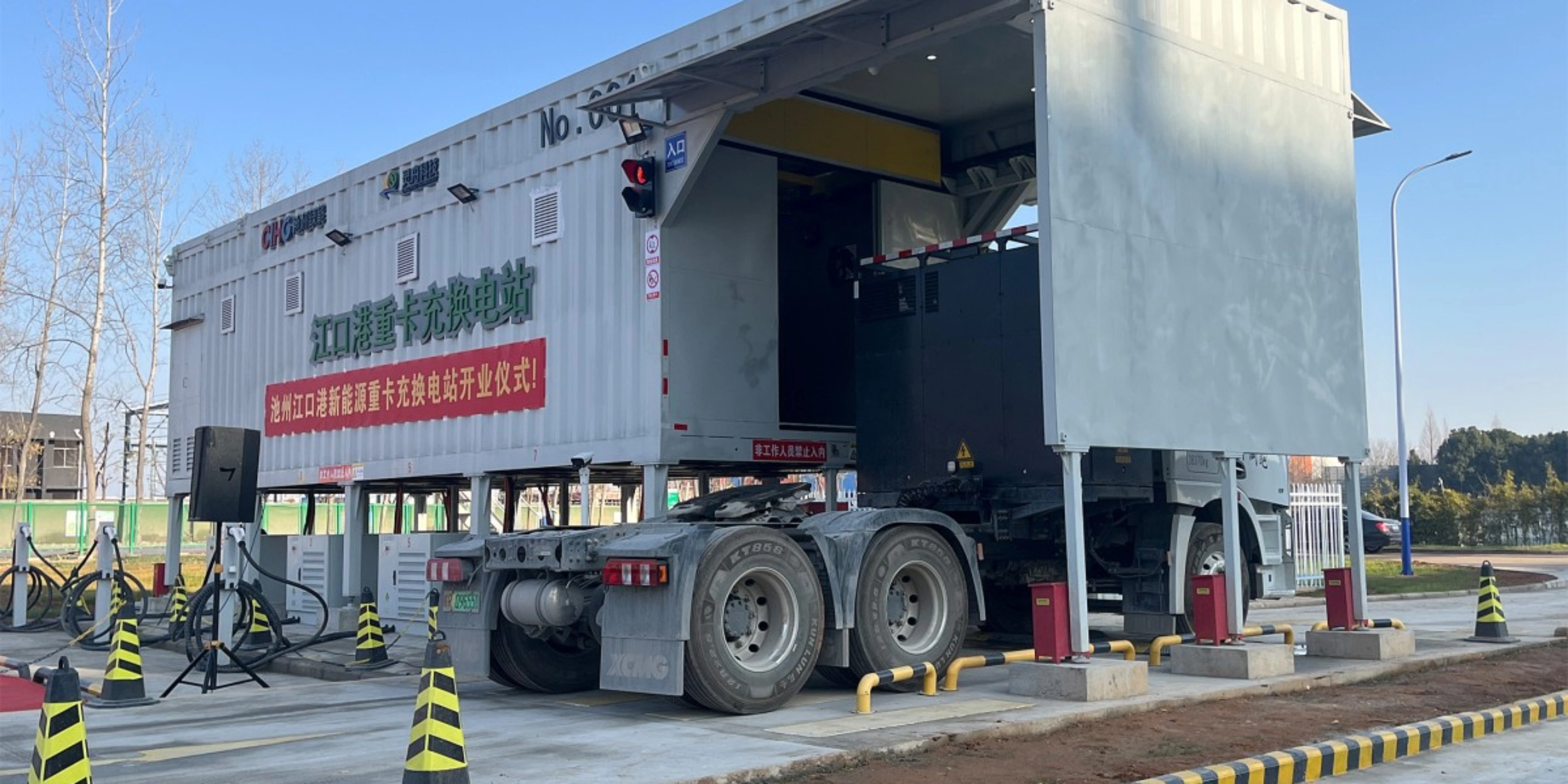 Truck at battery swap station with container module in industrial area.