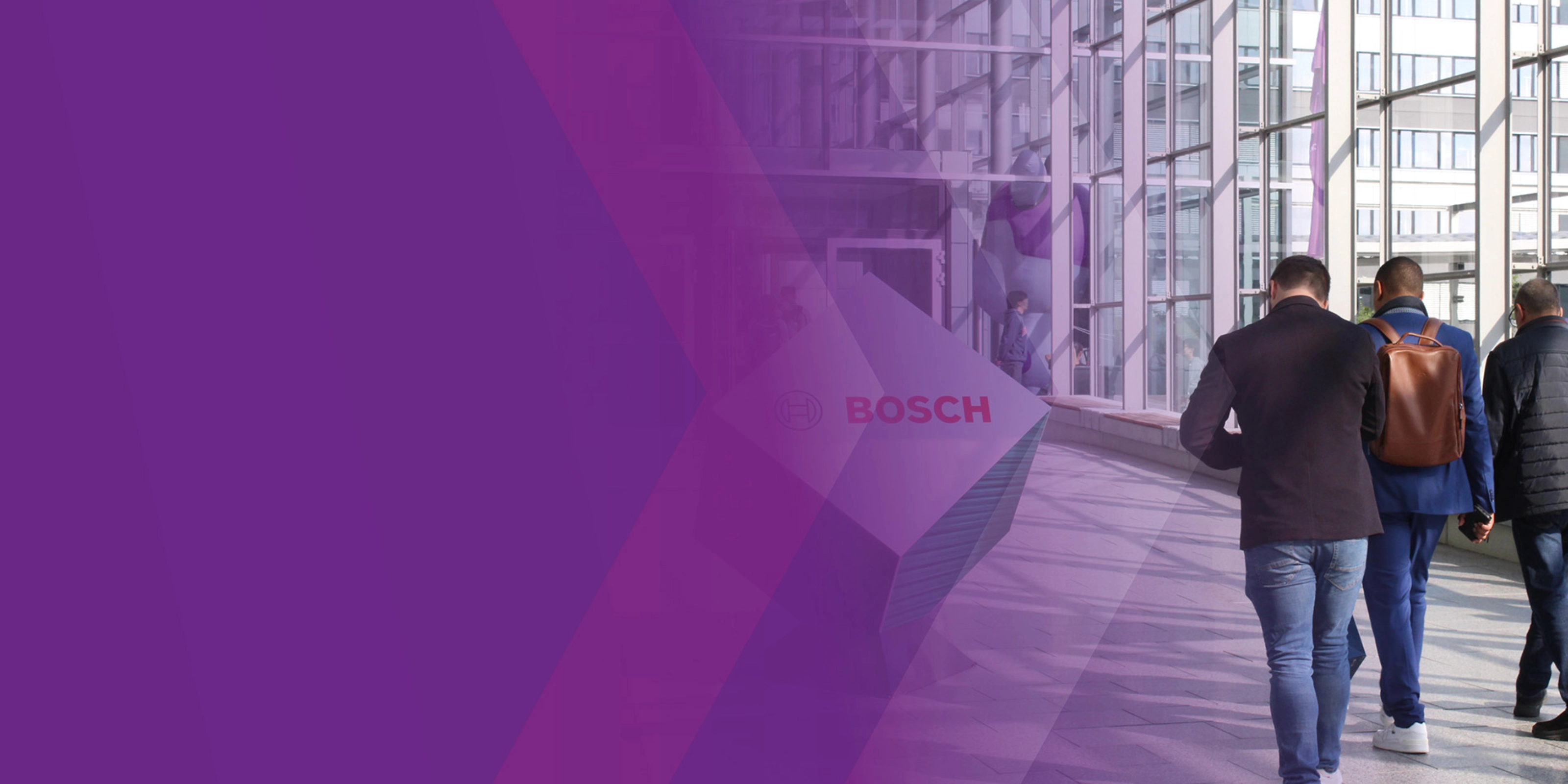 Three men walk through a modern glass corridor with a Bosch logo sign.