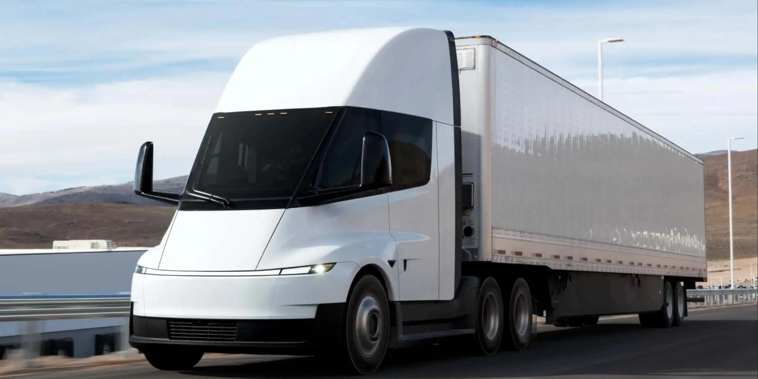 Electric semi-truck driving on a highway in a rural landscape.