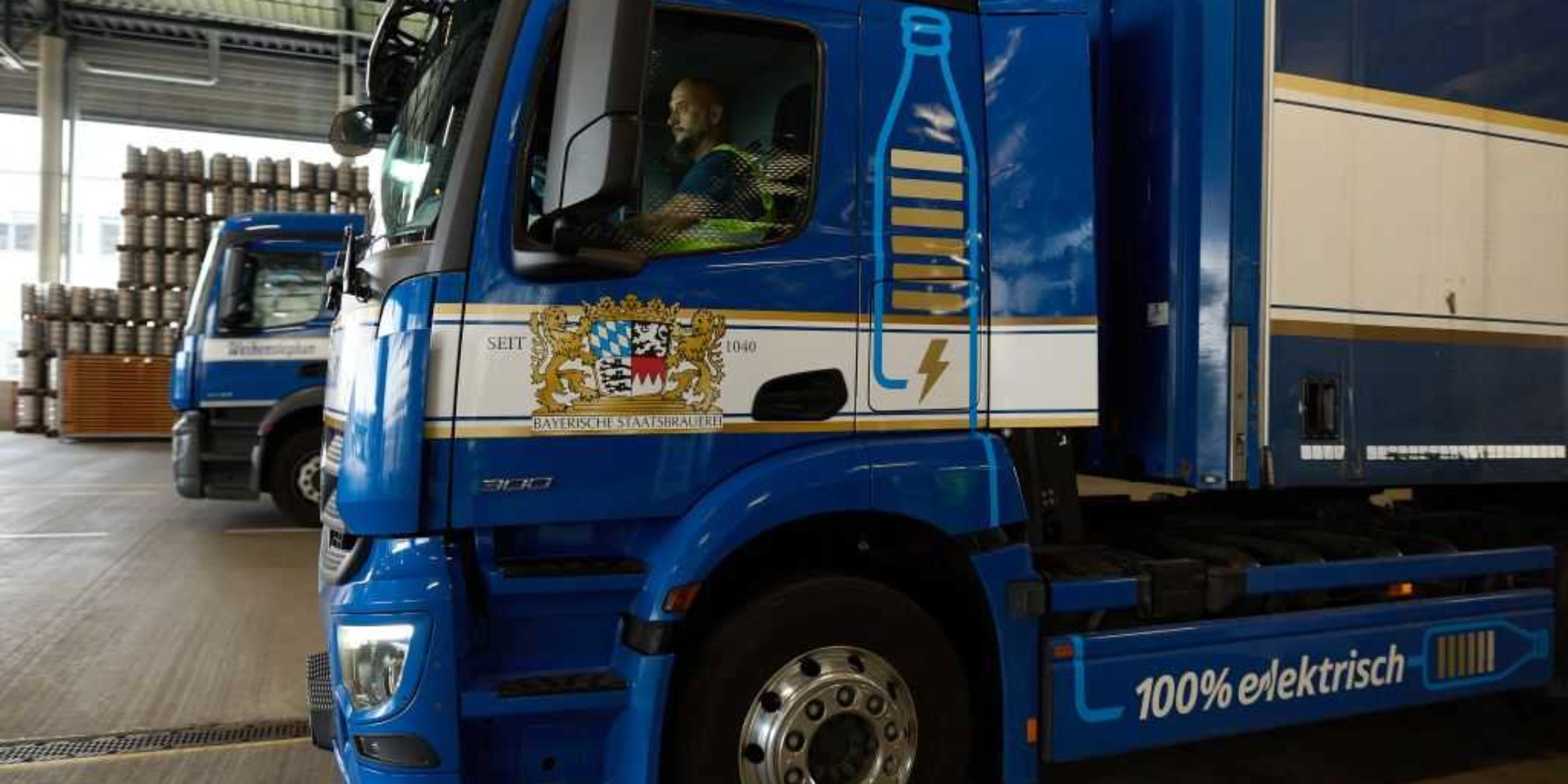Lastwagen steht in einer Logistikhalle, Fahrer sitzt im Führerhaus.