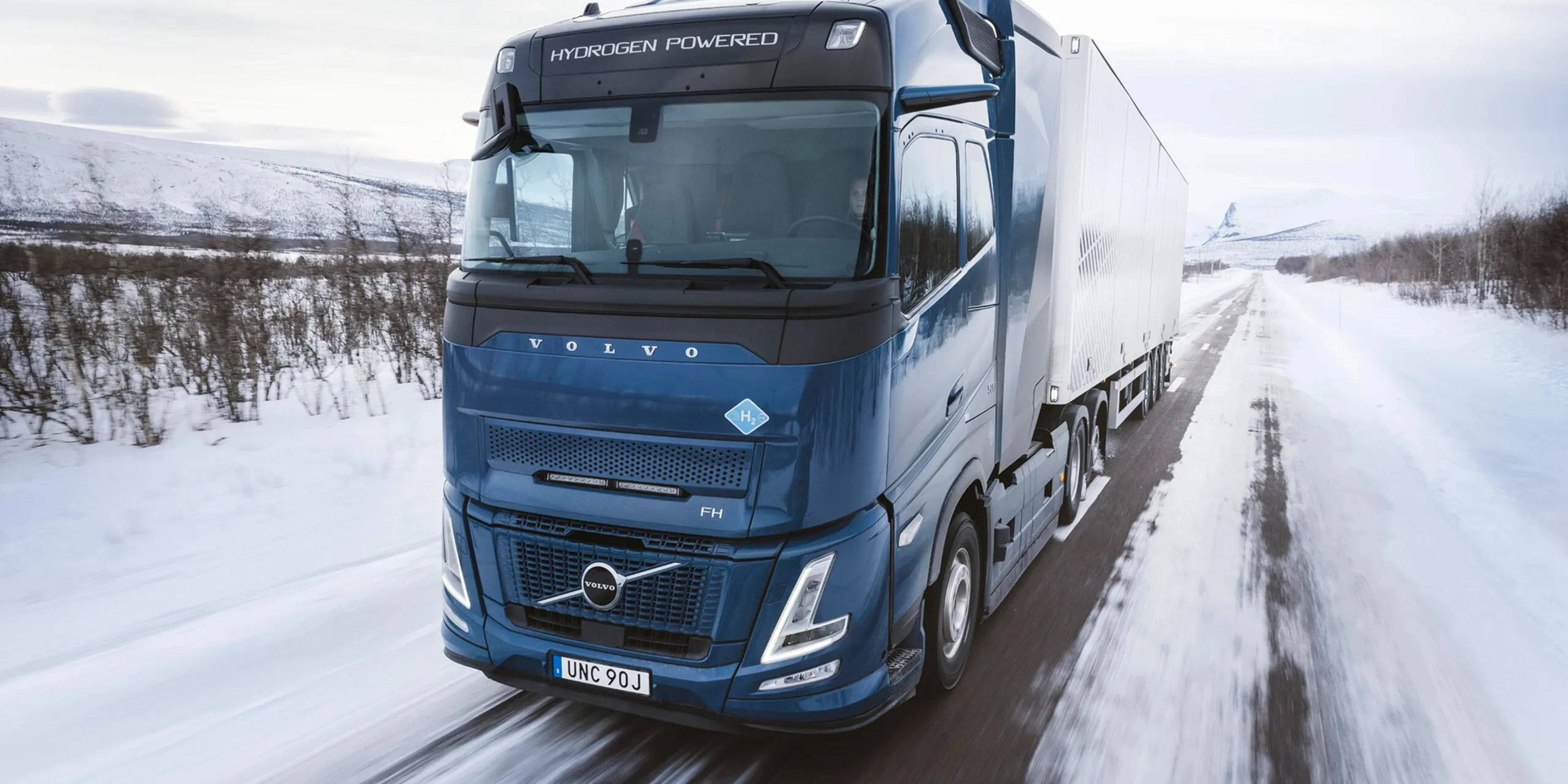 Wasserstoffbetriebener Volvo-Lkw fährt auf verschneiter Straße durch Winterlandschaft.