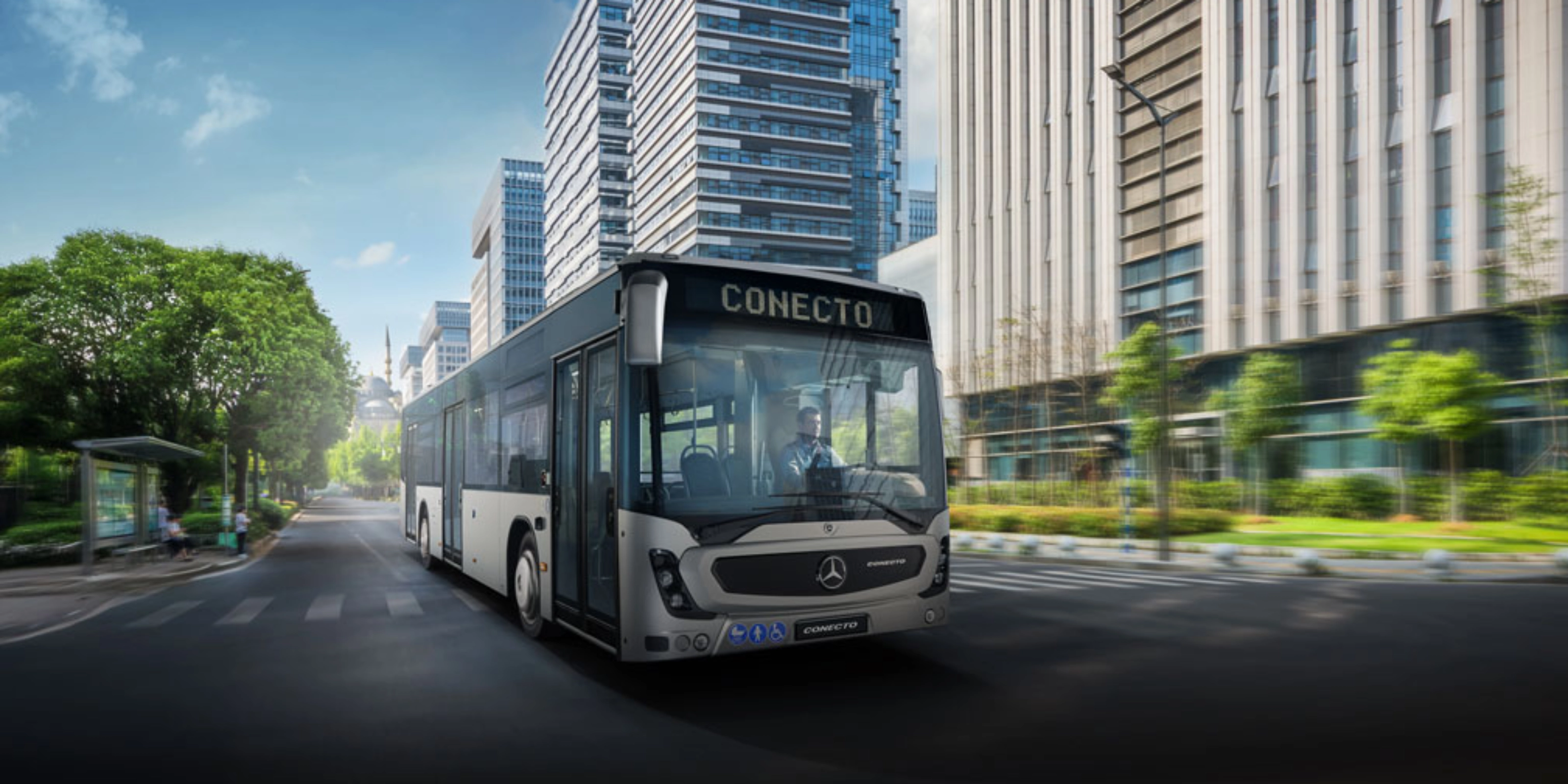 Modern city bus driving on a wide street between tall office buildings.