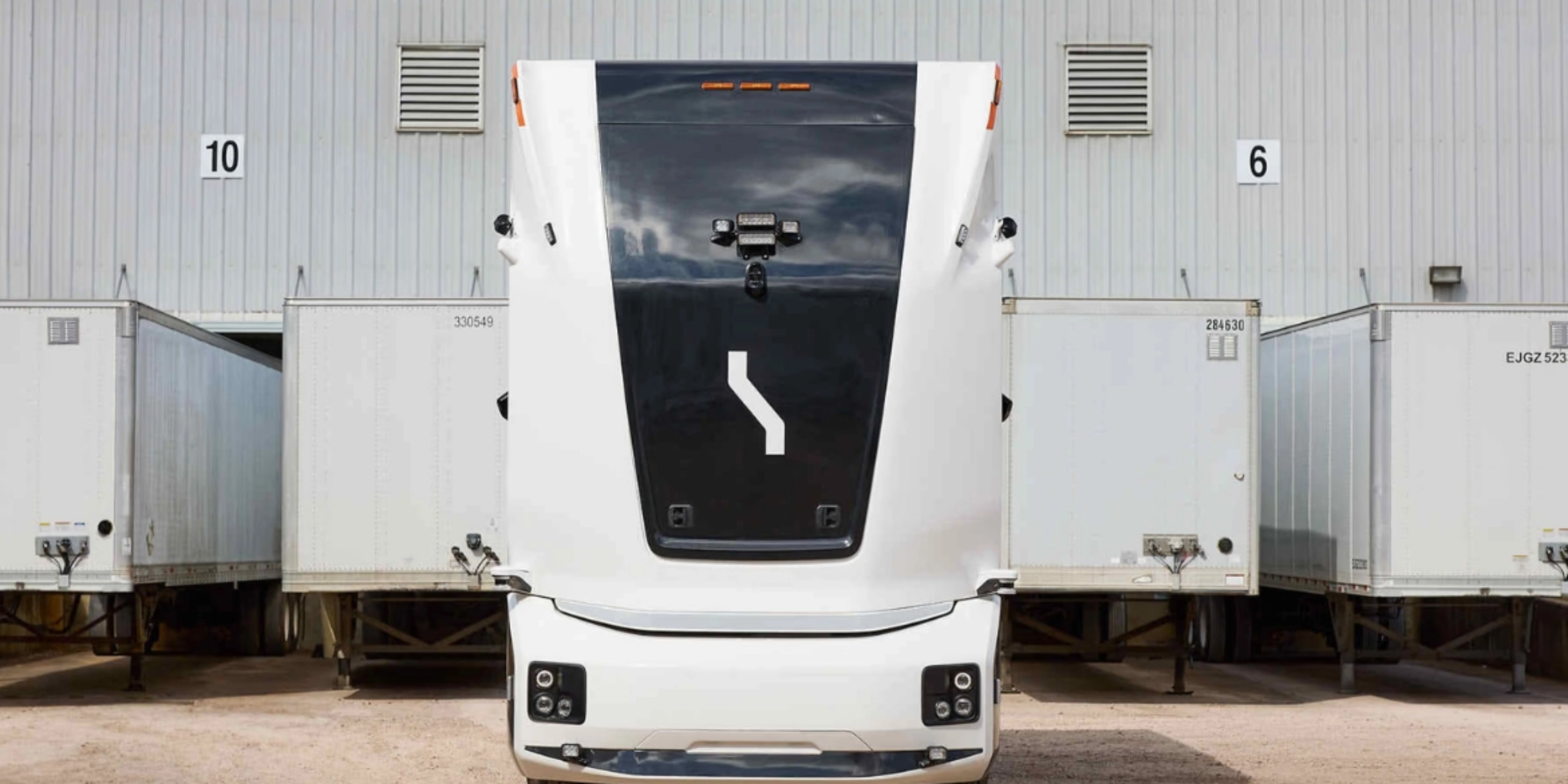 Einride autonomous electric truck in front of a warehouse with trailers.