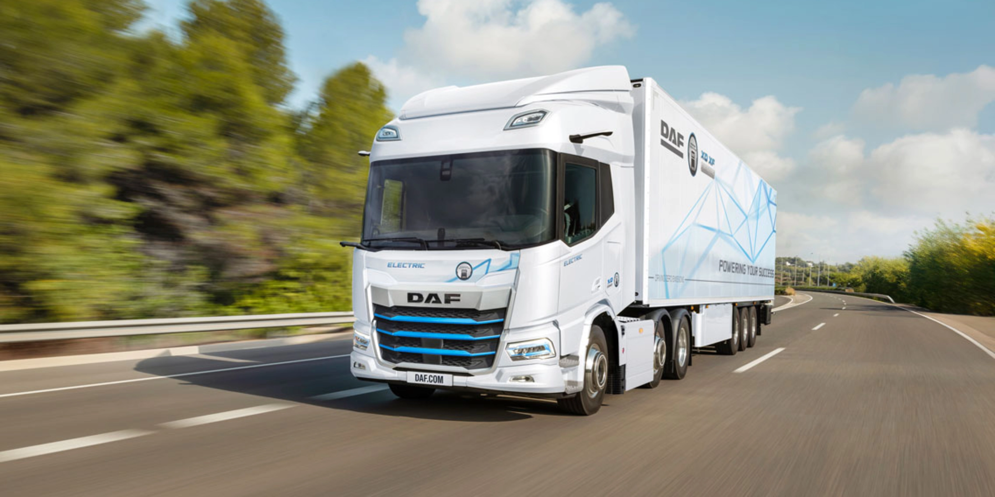 A white DAF electric truck is driving on a curved highway surrounded by greenery.
