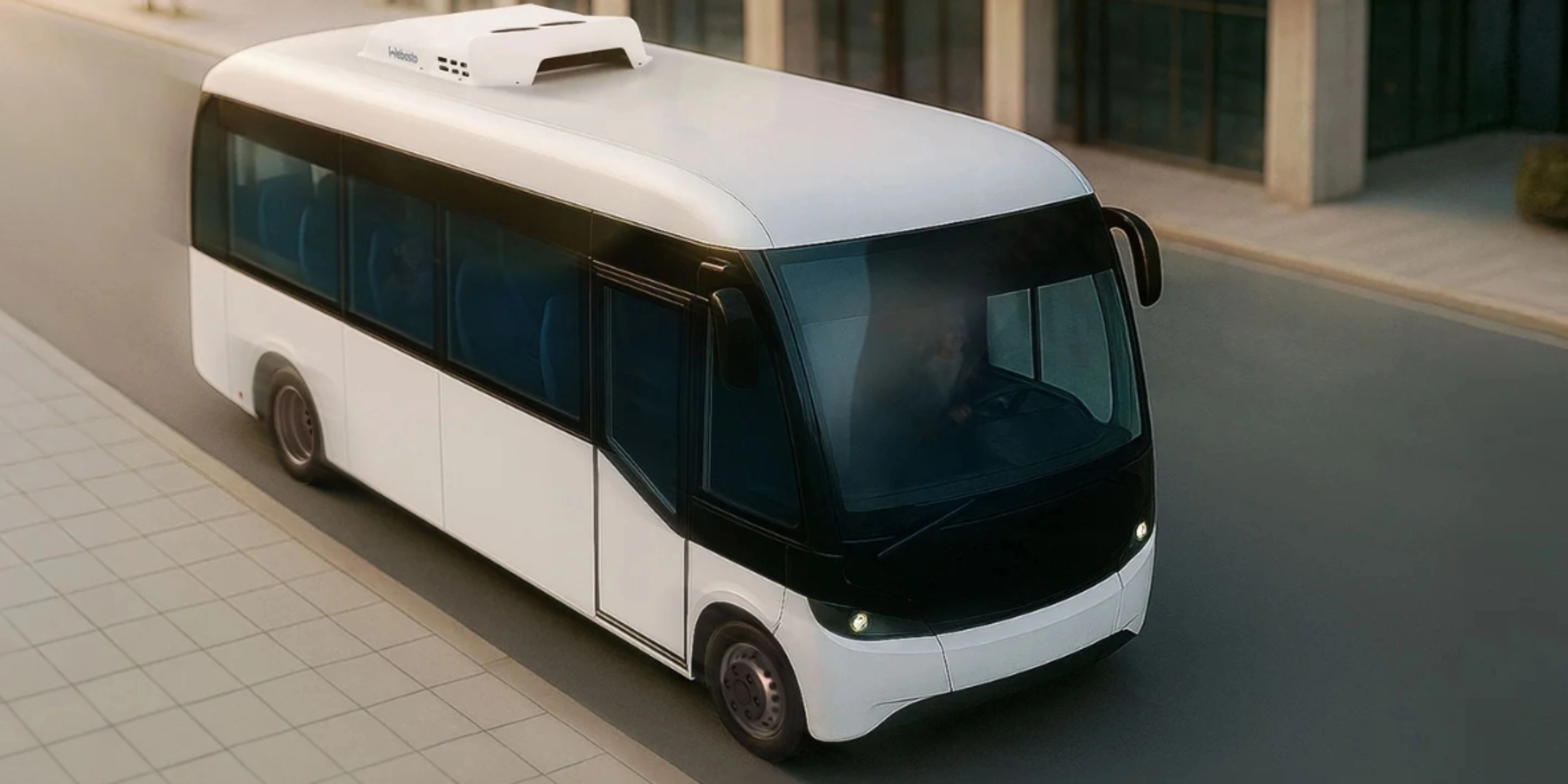Small white autonomous shuttle bus driving on a city street, viewed from above.