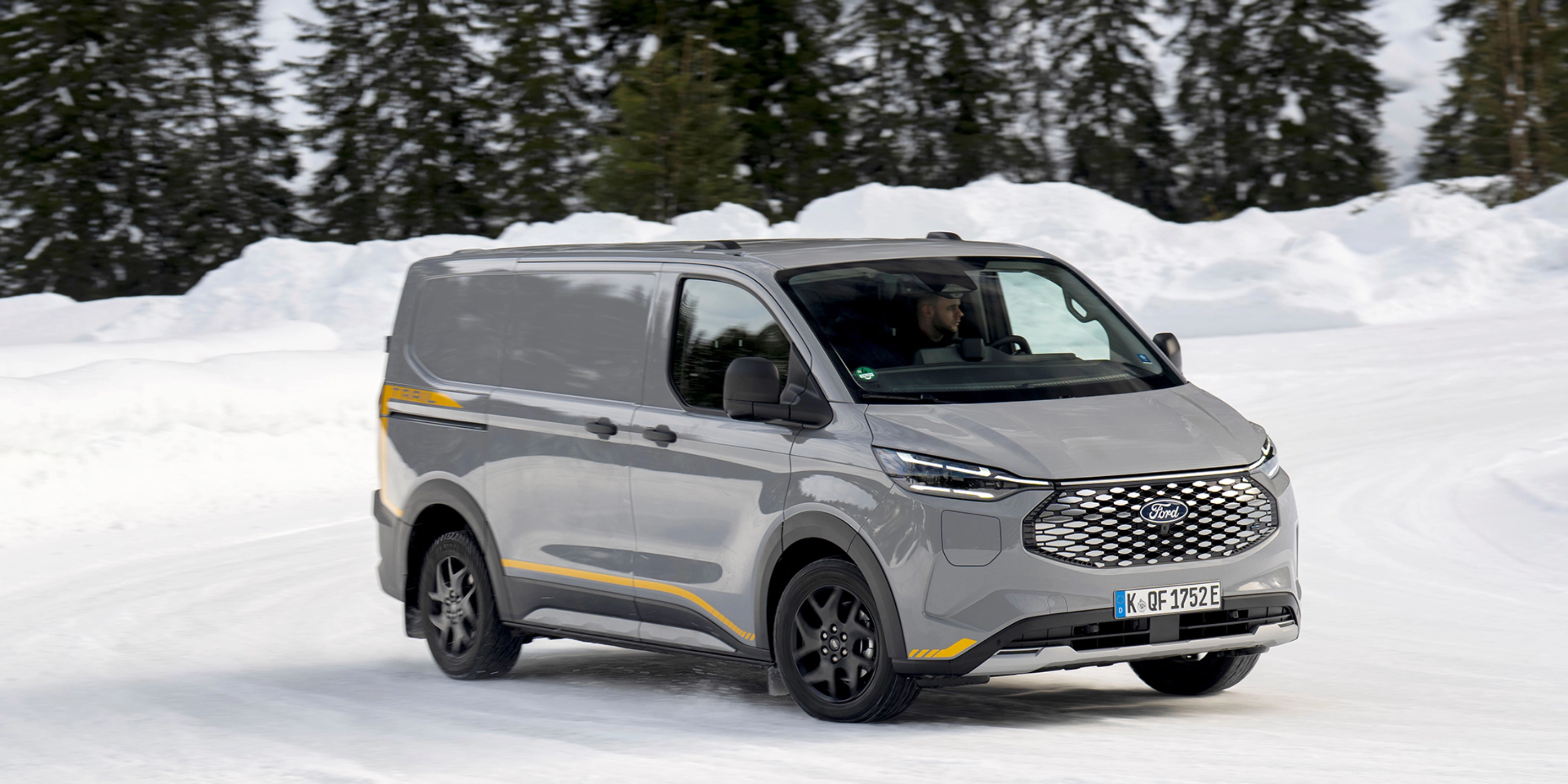 Grey Ford electric van driving on a snowy road with forest in the background.
