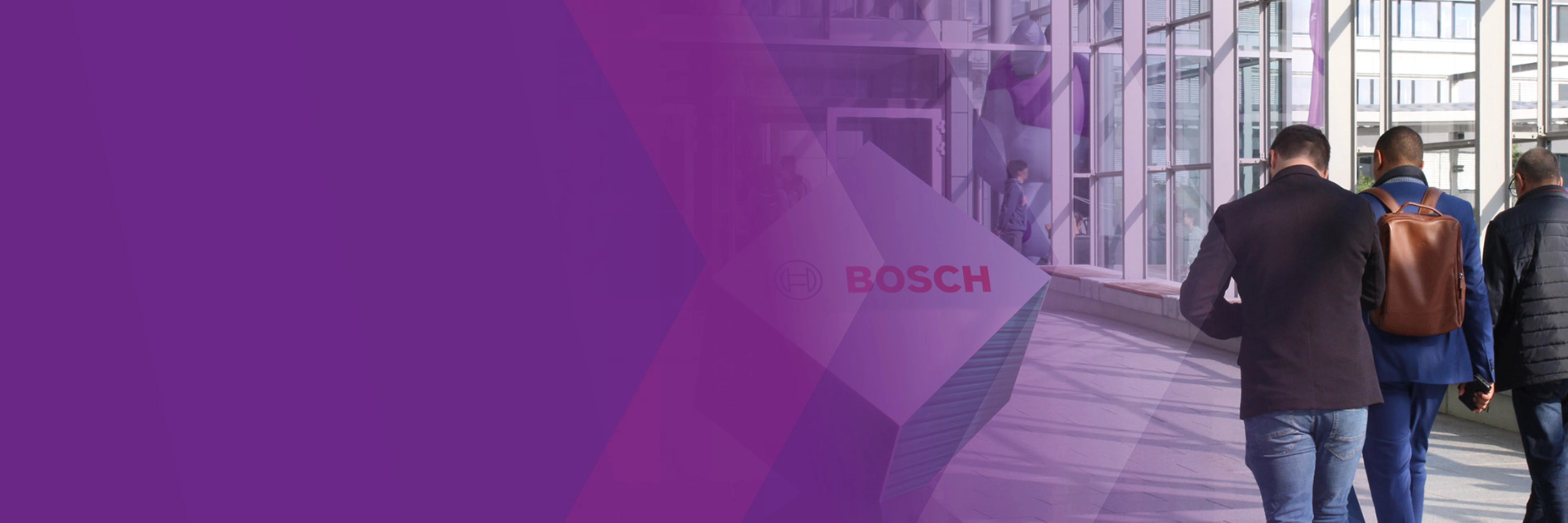 Three men walk through a modern glass corridor with a Bosch logo sign.