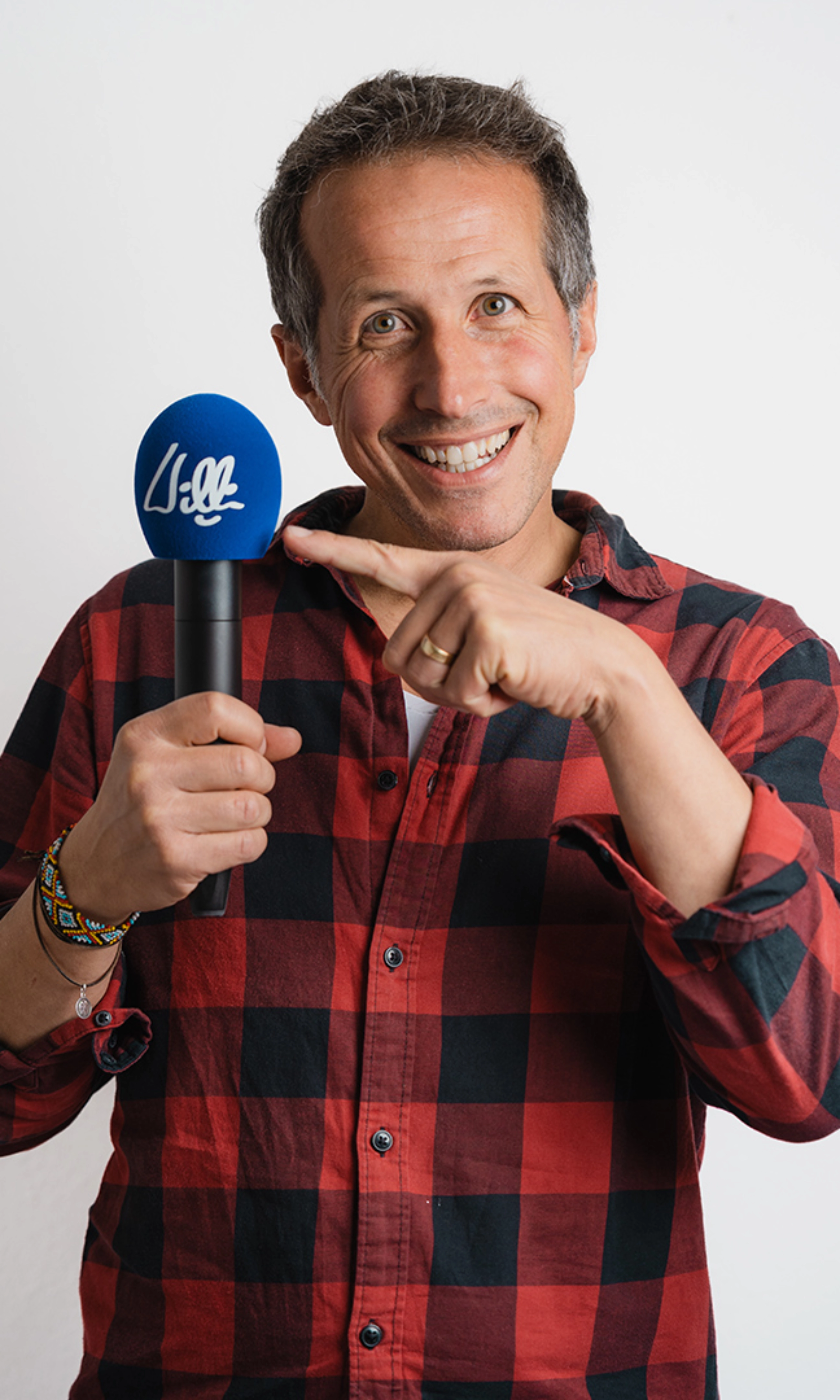 Willi Weitzel lächelt und zeigt in einem Porträt auf ein Mikrofon.