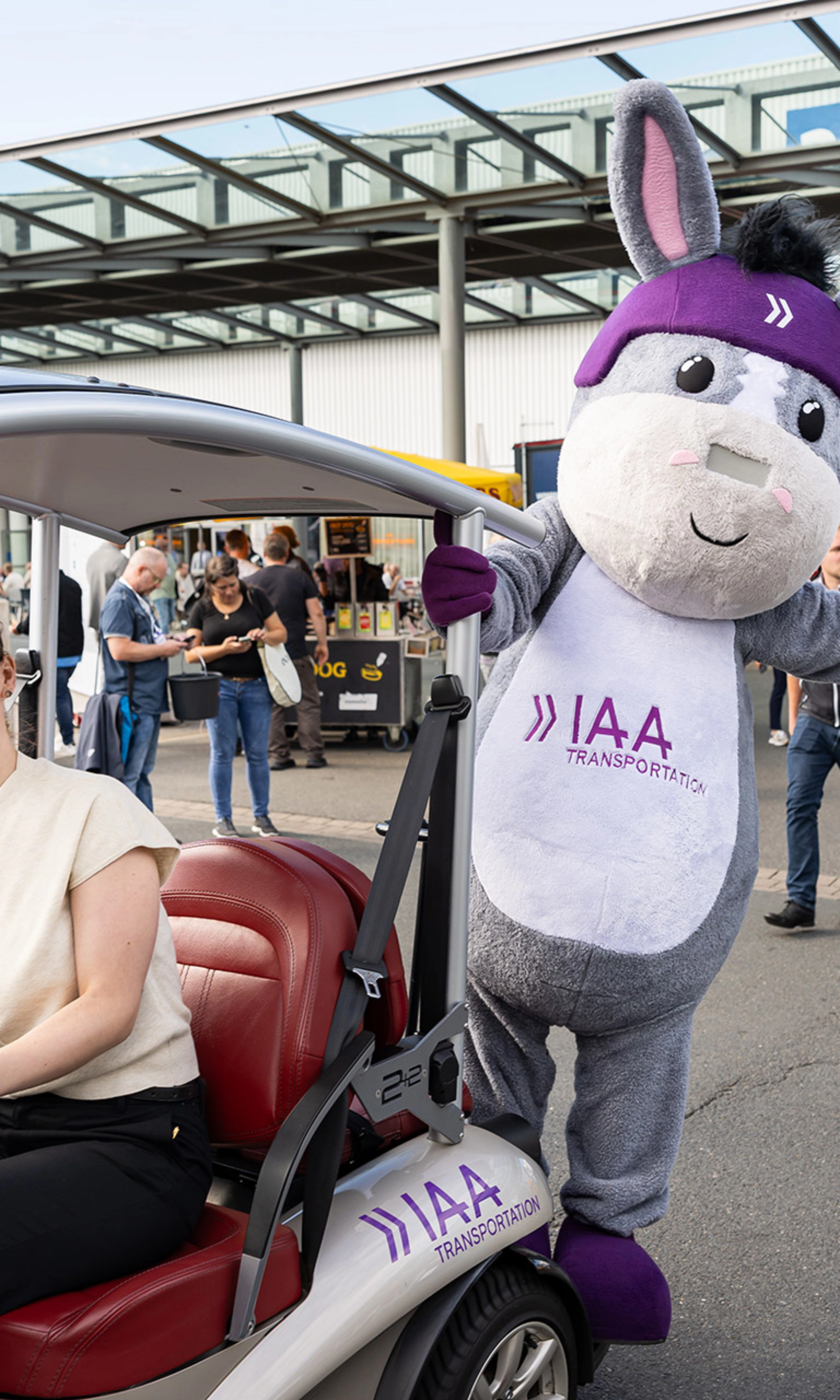 Woman in an IAA vehicle next to the IAA Transportation mascot at the event.