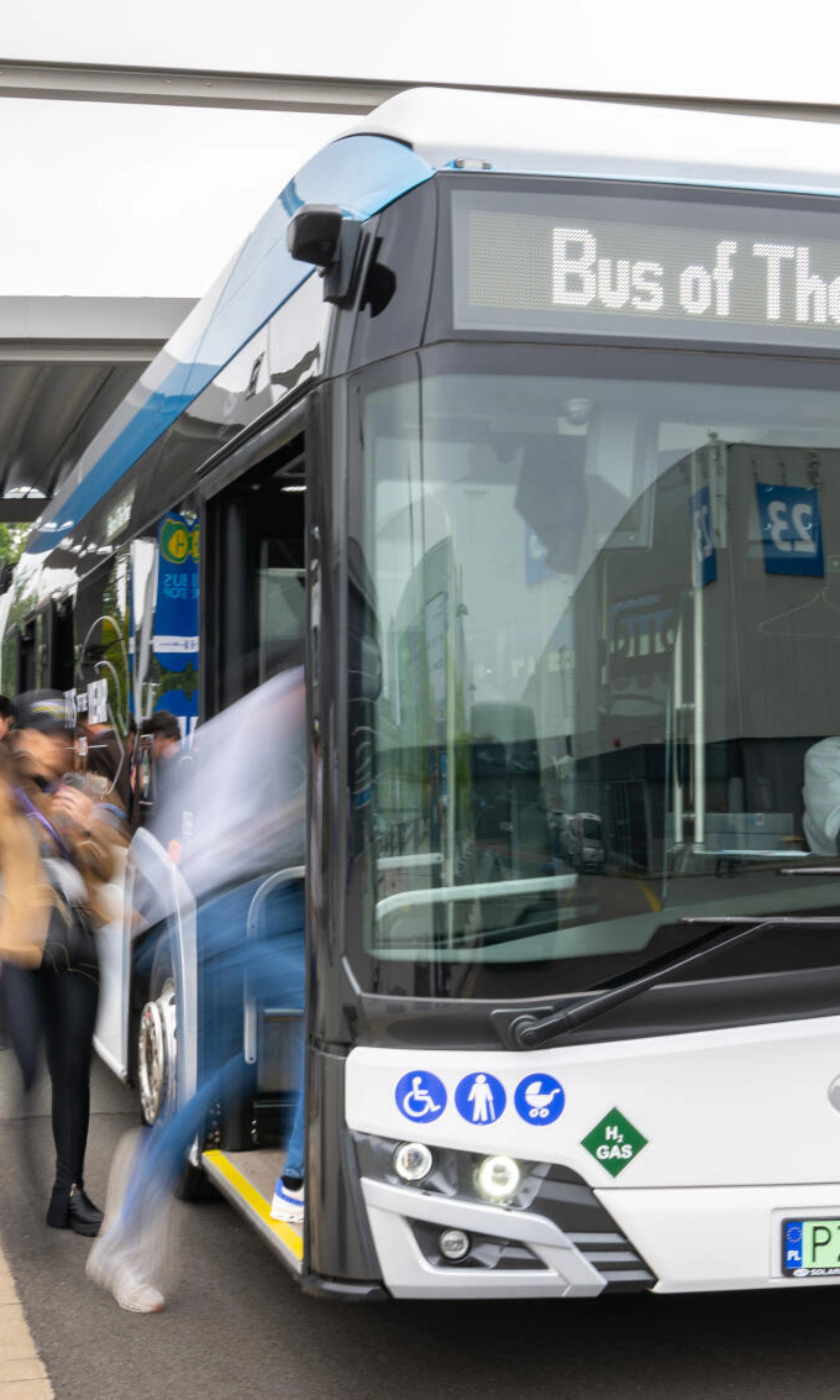 Hydrogen shuttle bus marked “Bus of The Year 2025” at a busy bus stop.