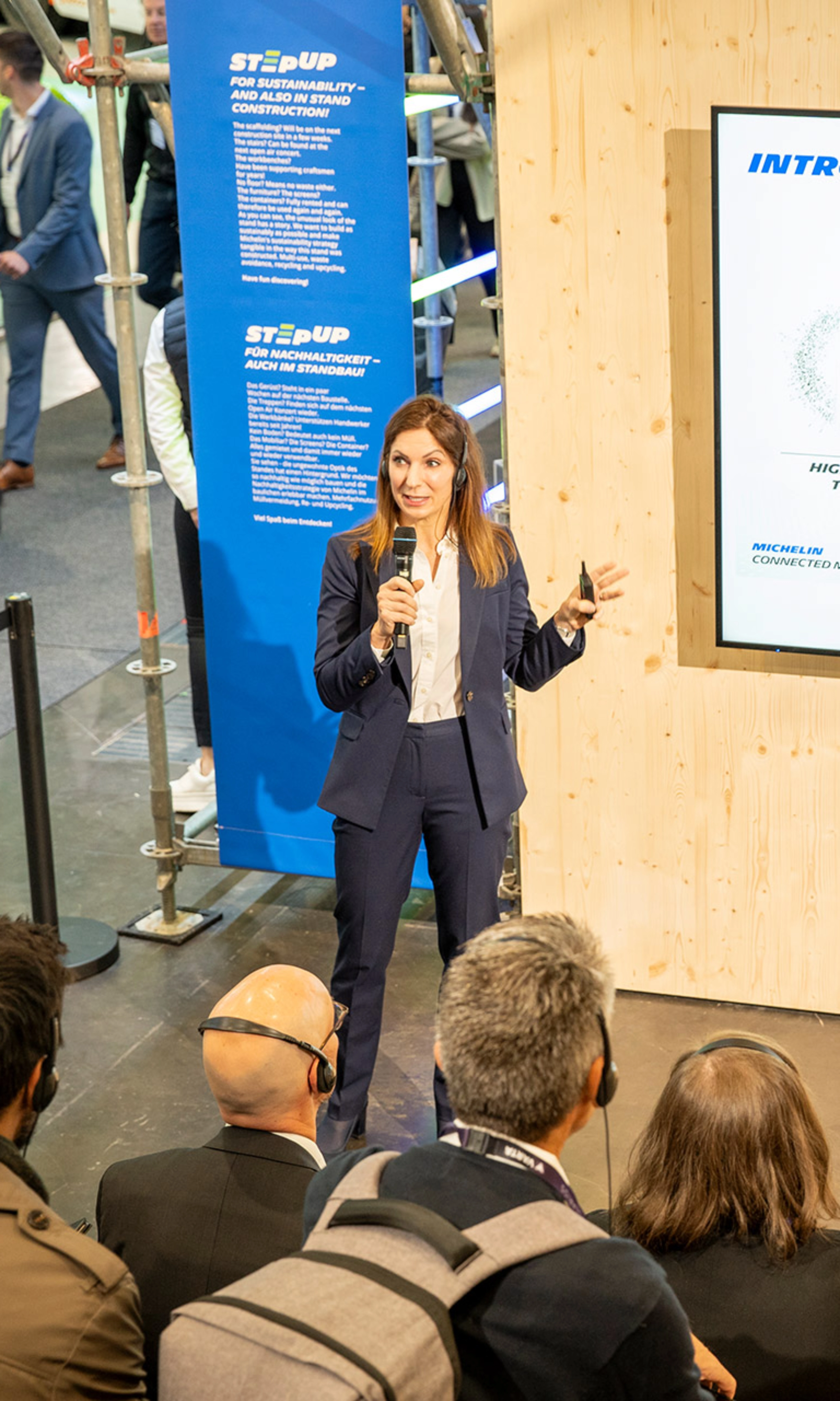Woman presents Michelin Connected Mobility to audience at trade fair booth.