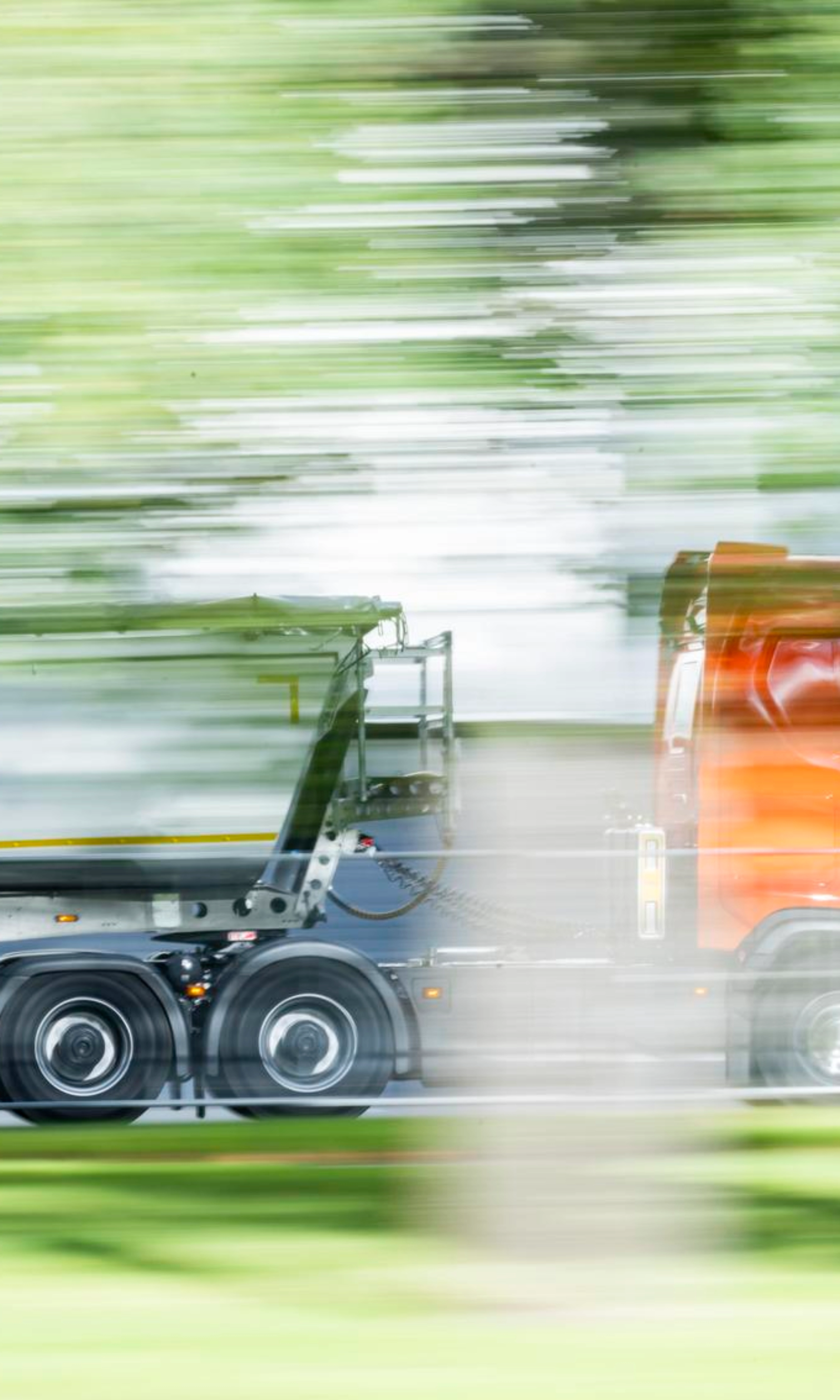 Ein Lkw mit Auflieger fährt auf einer von Grün umgebenen Straße.