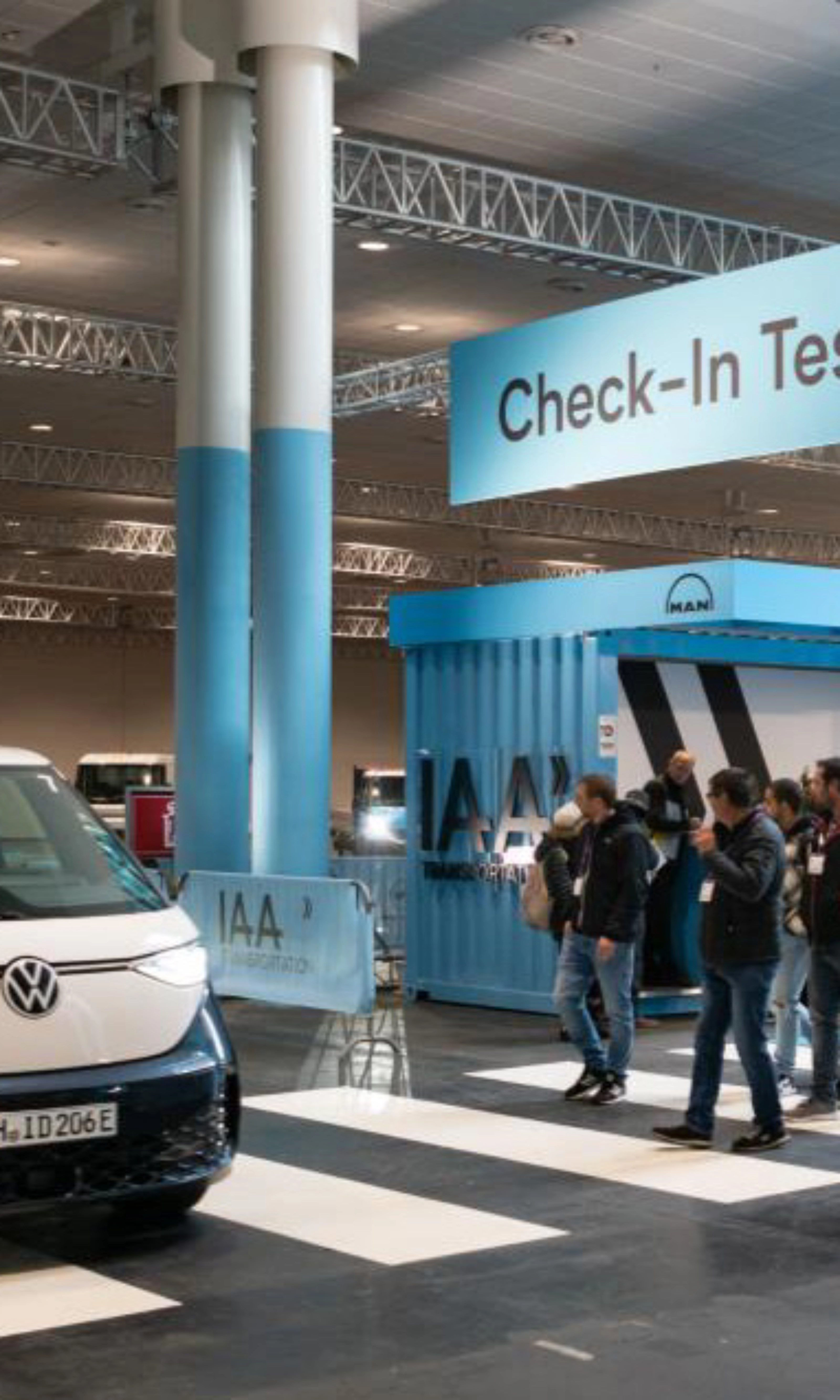 Exhibition hall scene with a Volkswagen van driving past the IAA Transportation check-in for test drives.