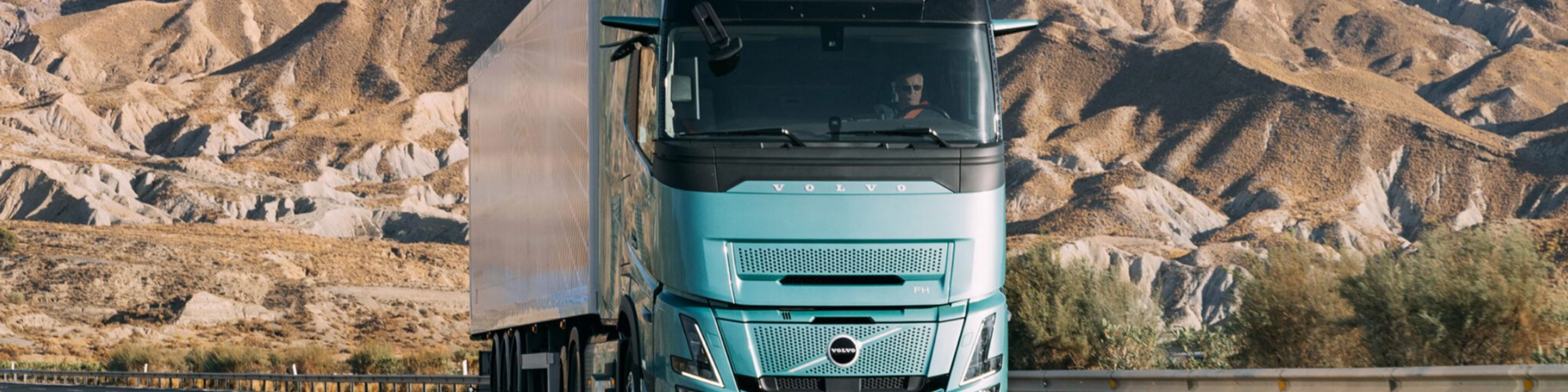 Volvo truck driving on a highway through a rocky desert landscape.