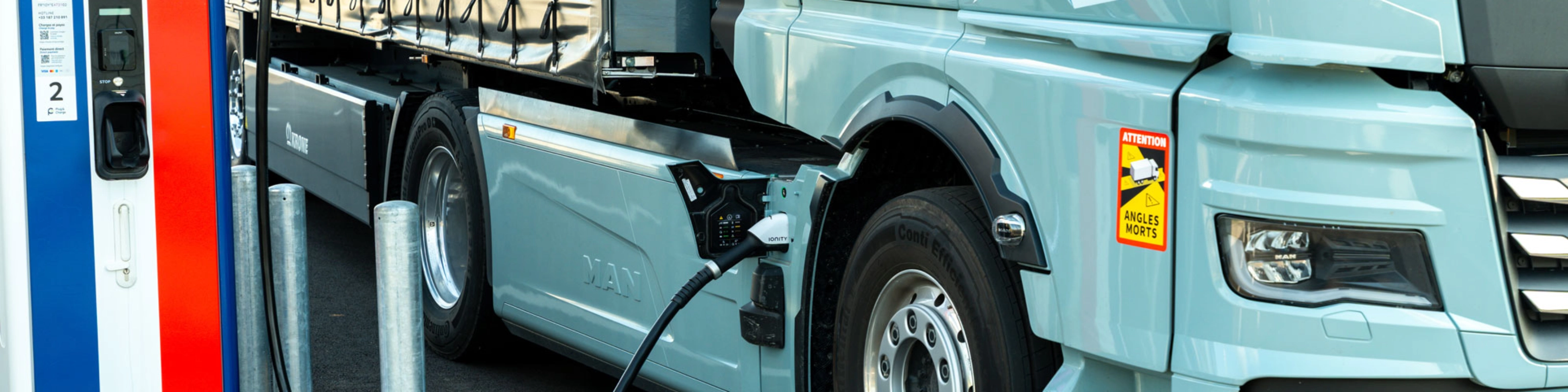 Electric truck charging at a public station, labeled 100% electric.