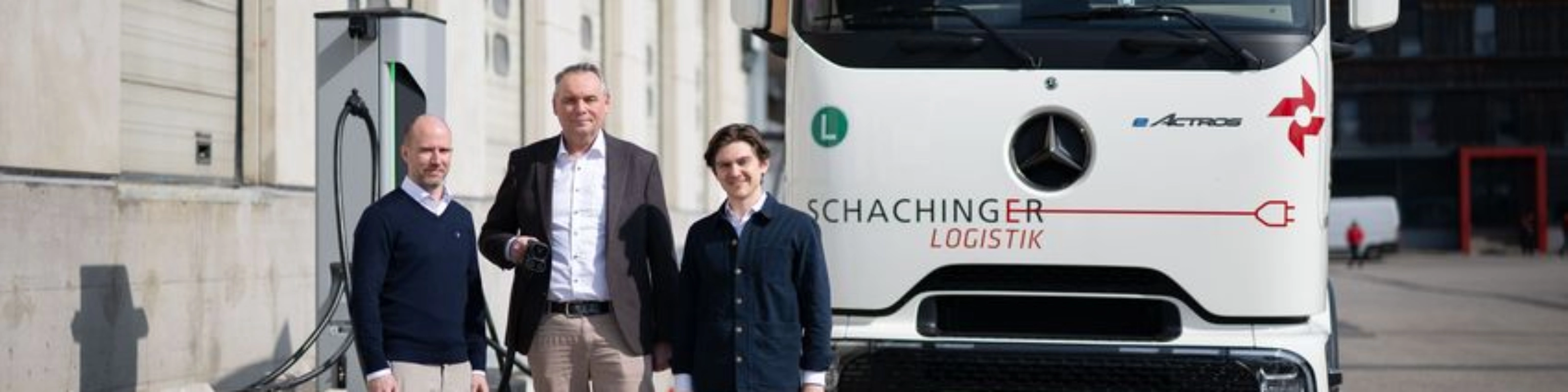 Three men standing in front of a white truck outside an industrial building.