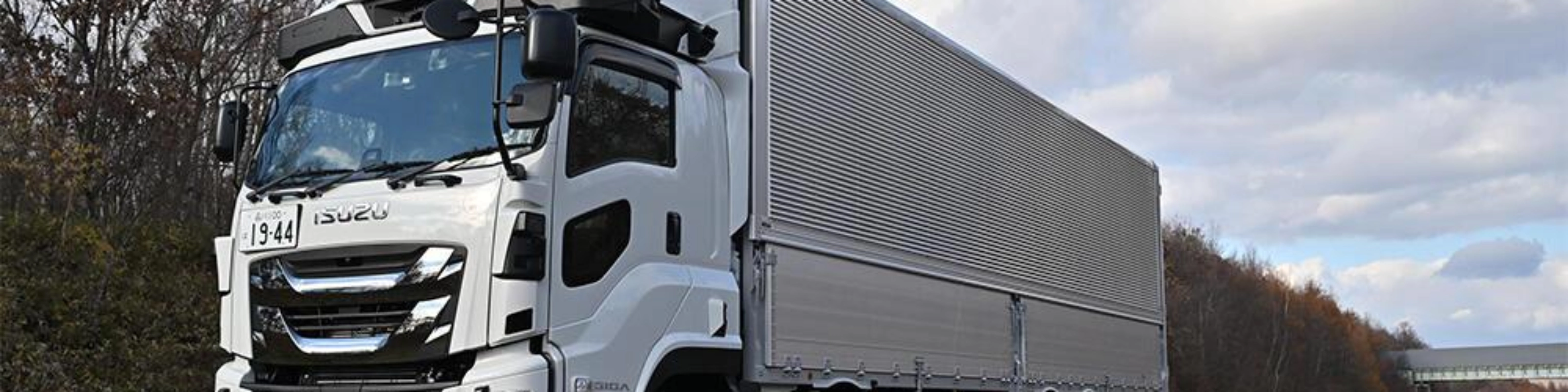 White semi-truck with trailer driving on a highway under a cloudy sky.