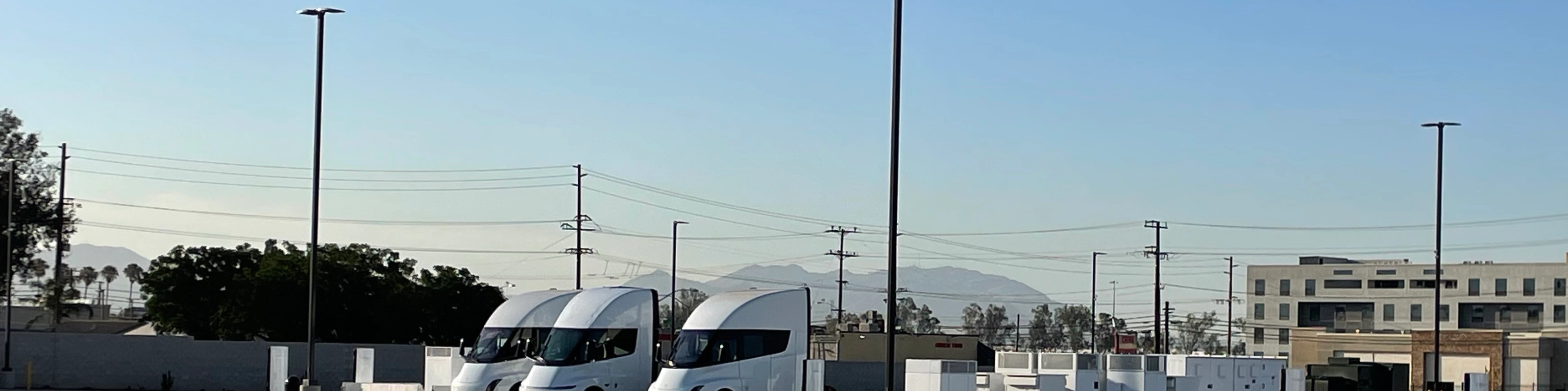 Three white electric trucks are parked at a charging station.