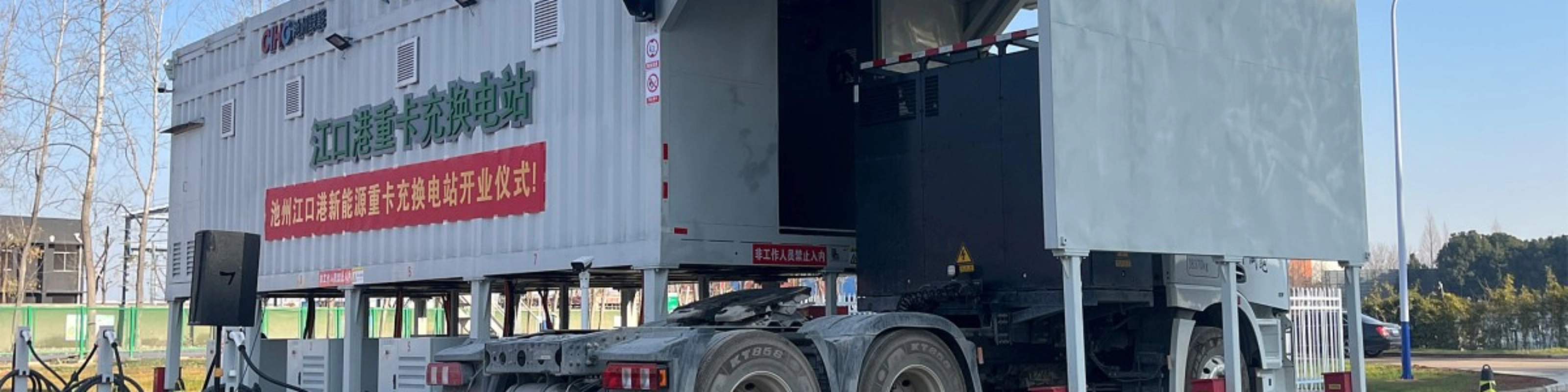 Truck at battery swap station with container module in industrial area.