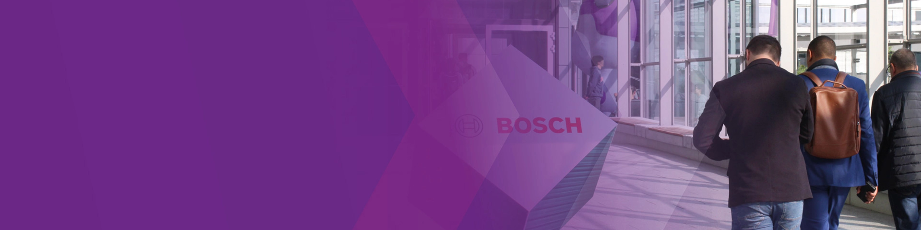 Three men walk through a modern glass corridor with a Bosch logo sign.