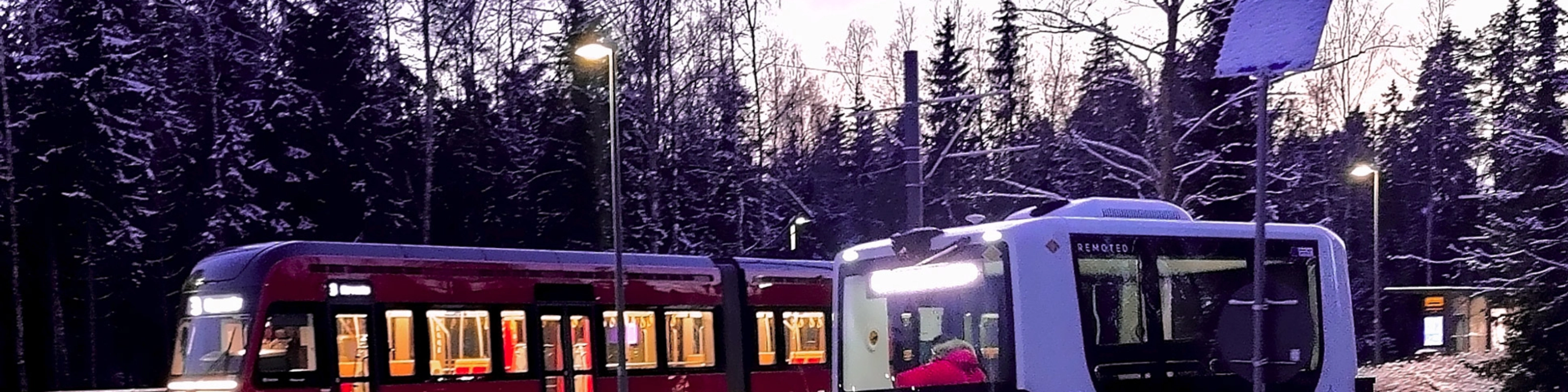 Autonomous shuttle bus driving beside a tram on a snowy street.