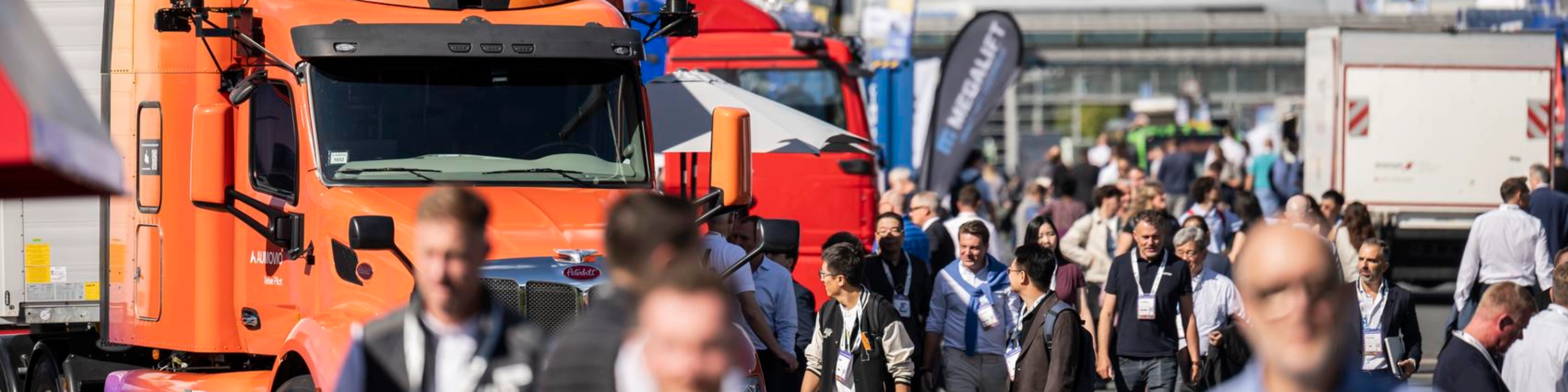 Besucher gehen auf einem belebten Messegelände zwischen Lkw hindurch.