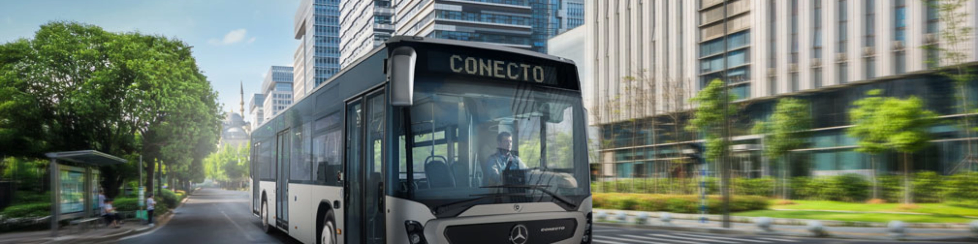 Modern city bus driving on a wide street between tall office buildings.