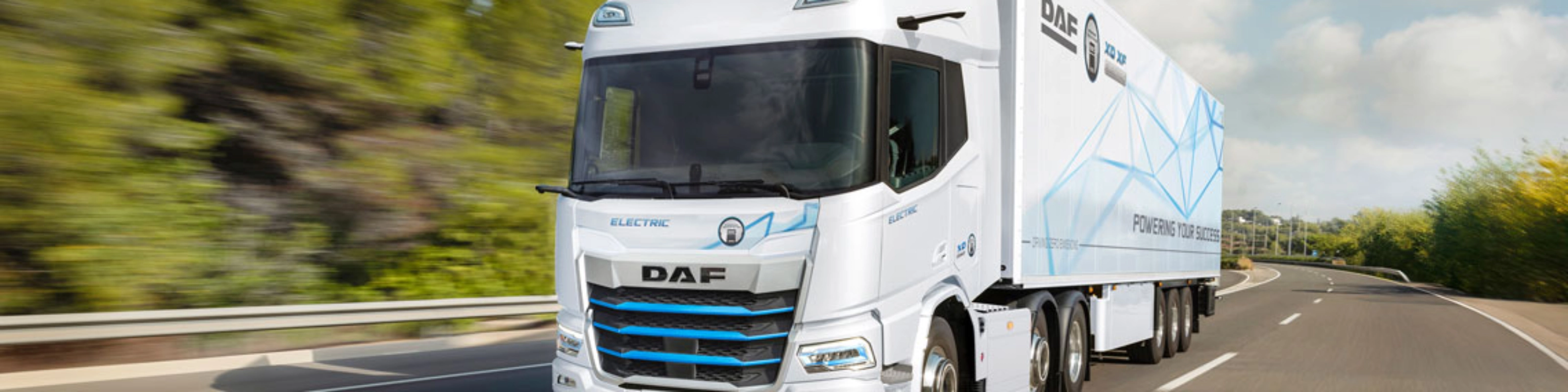 A white DAF electric truck is driving on a curved highway surrounded by greenery.