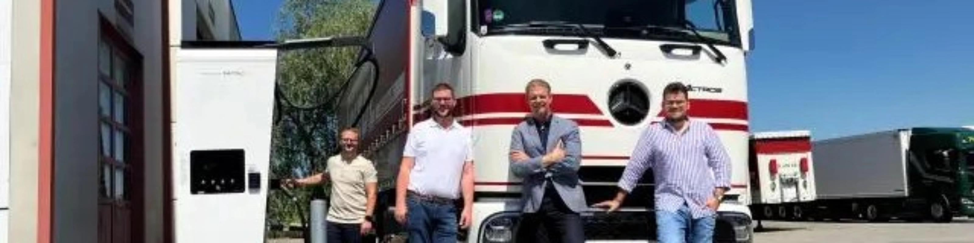 Vier Männer stehen vor einem weißen Frigel Lkw.