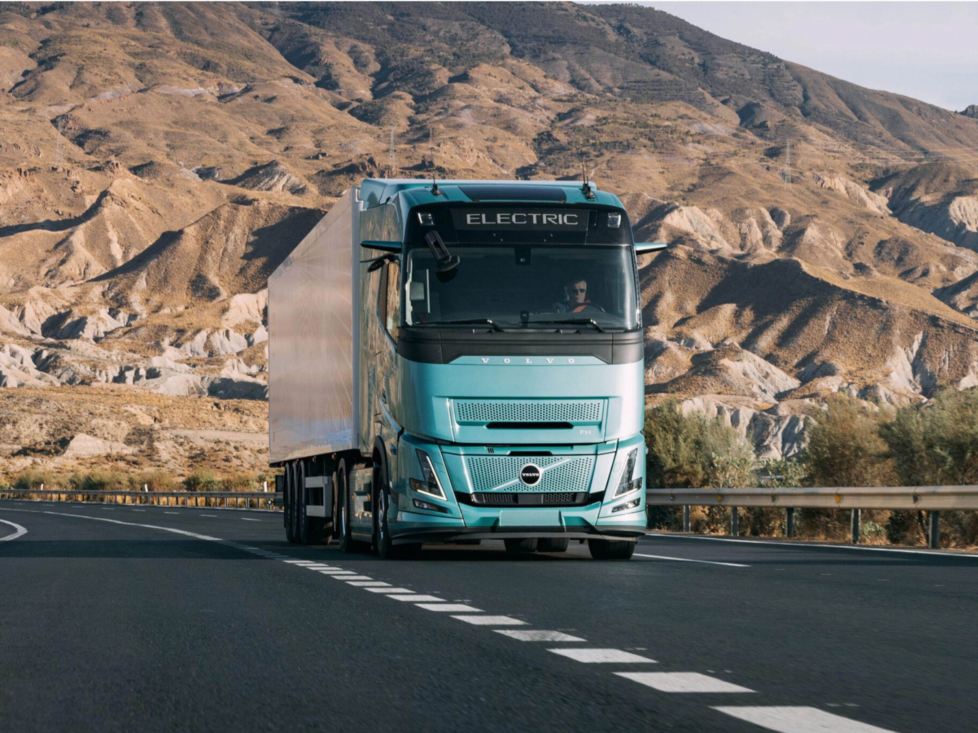 Volvo truck driving on a highway through a rocky desert landscape.