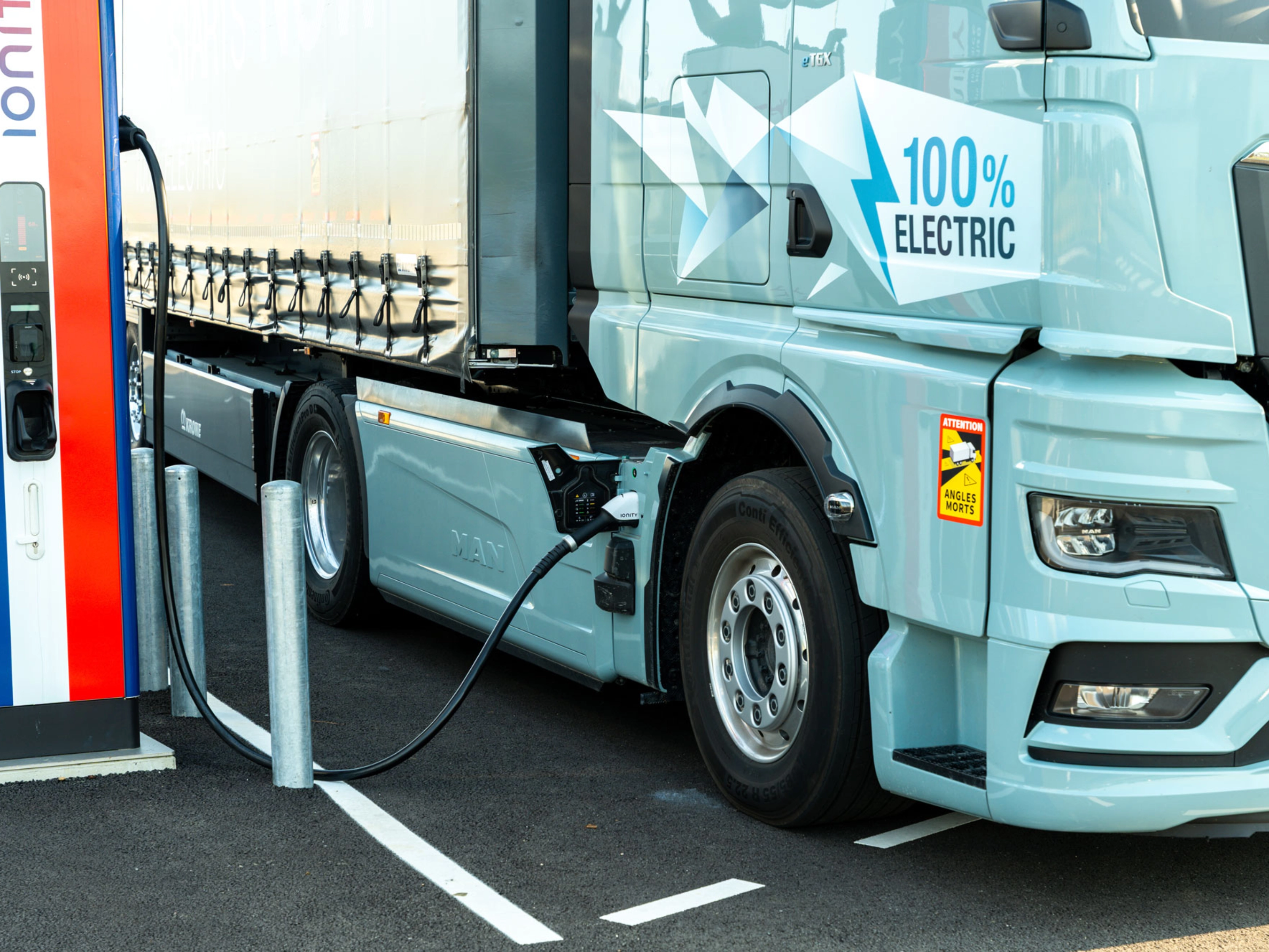 Electric truck charging at a public station, labeled 100% electric.