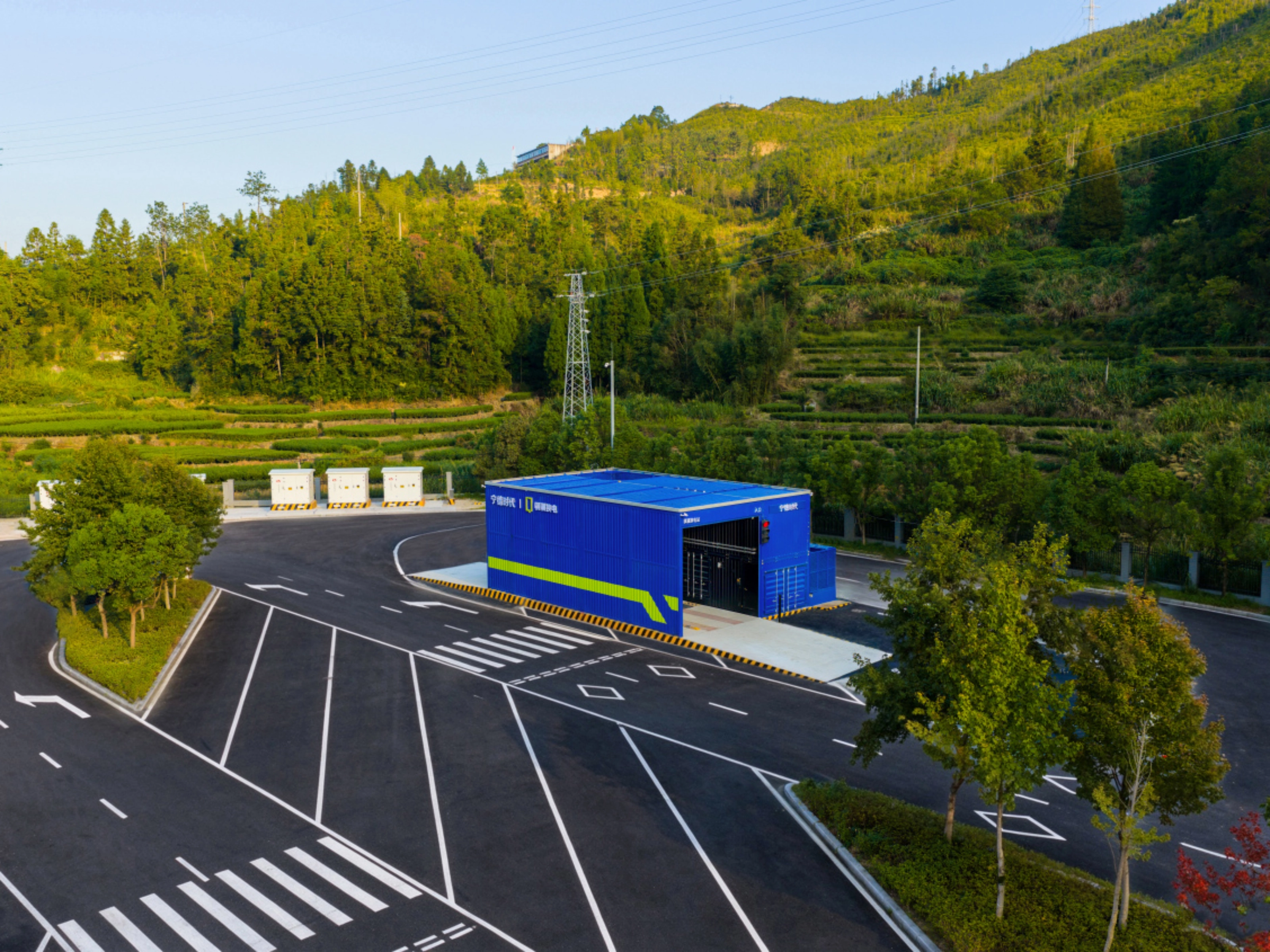 Teststrecke mit Fahrbahnmarkierungen und blauem Gebäude, umgeben von Bäumen und bewaldeten Hügeln.