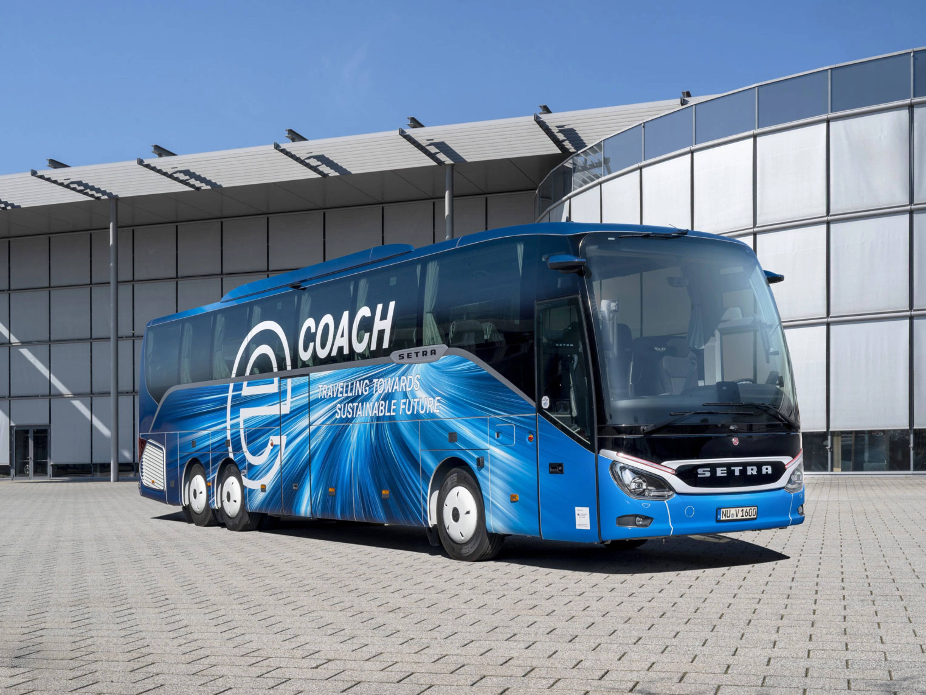 Blauer Setra-Reisebus mit Nachhaltigkeits-Slogan vor modernem Gebäude.