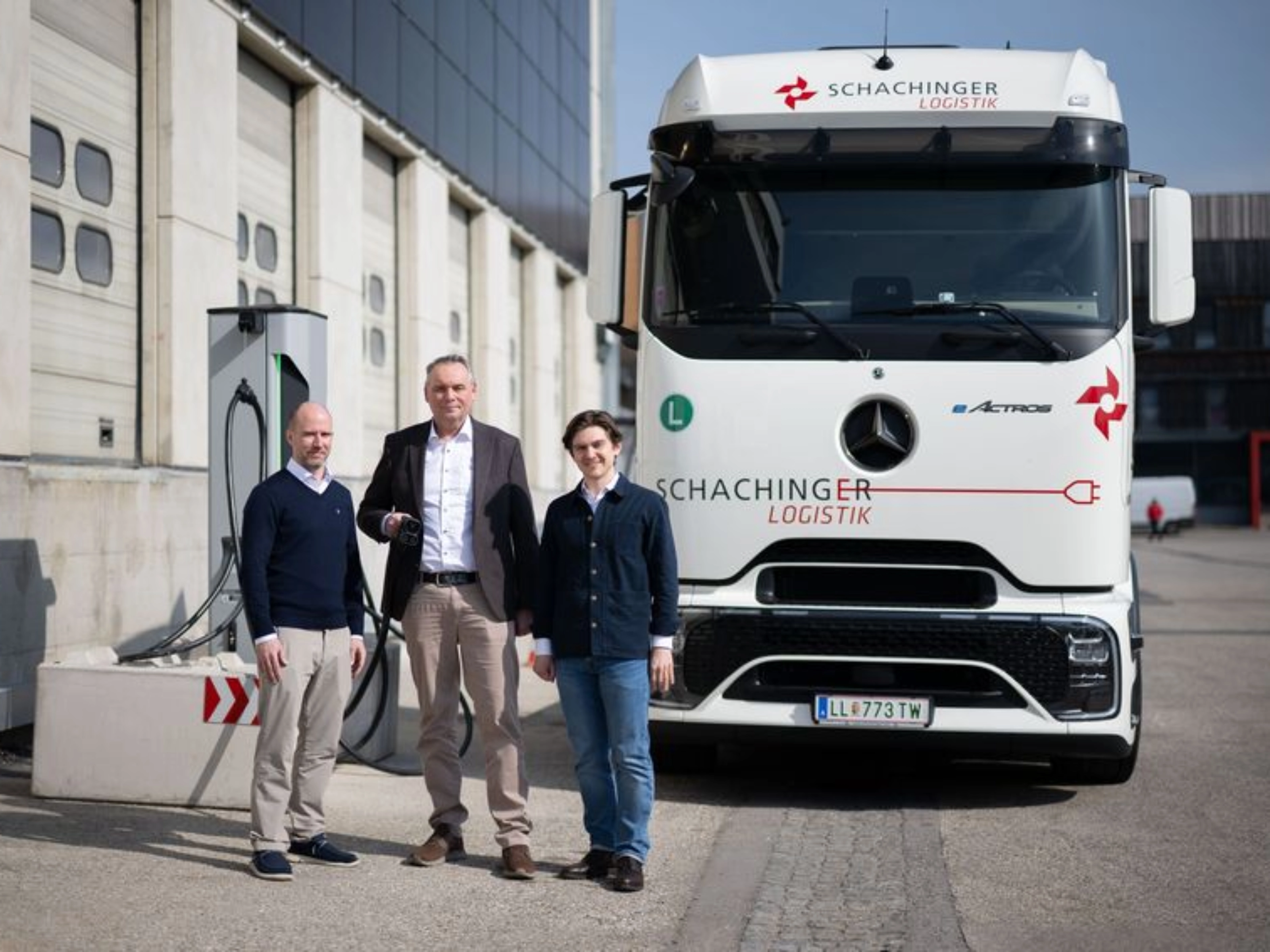 Three men standing in front of a white truck outside an industrial building.