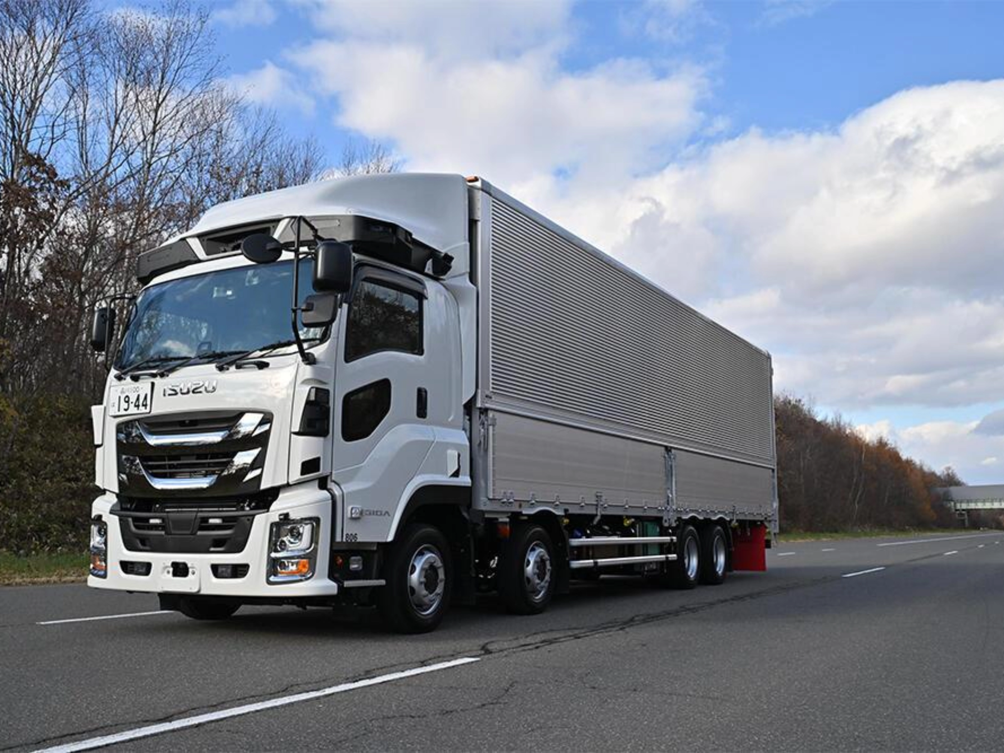 White semi-truck with trailer driving on a highway under a cloudy sky.