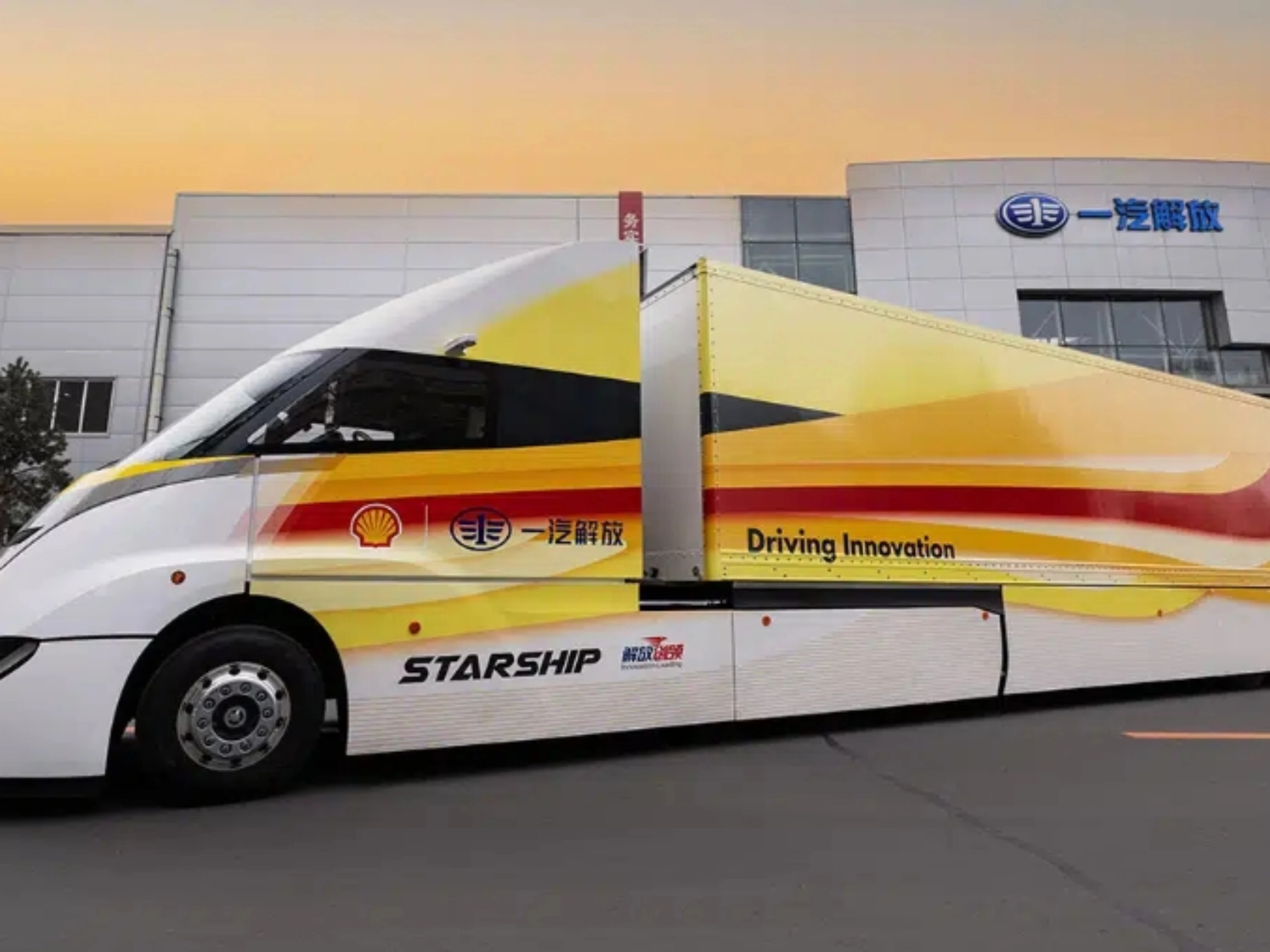 Weißer STARSHIP-Bus mit roten und gelben Streifen vor einem Industriegebäude bei Sonnenuntergang.