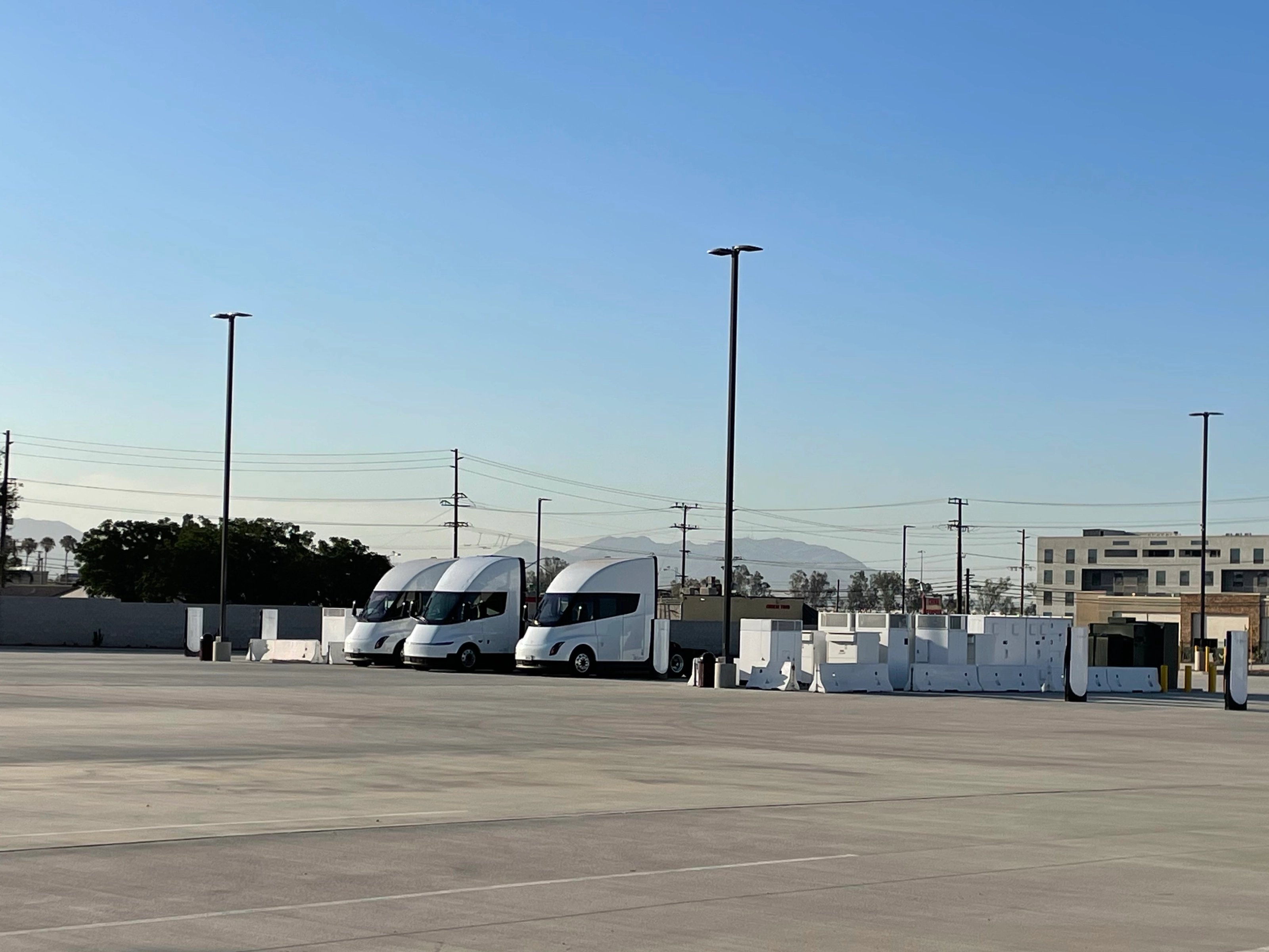 Three white electric trucks are parked at a charging station.